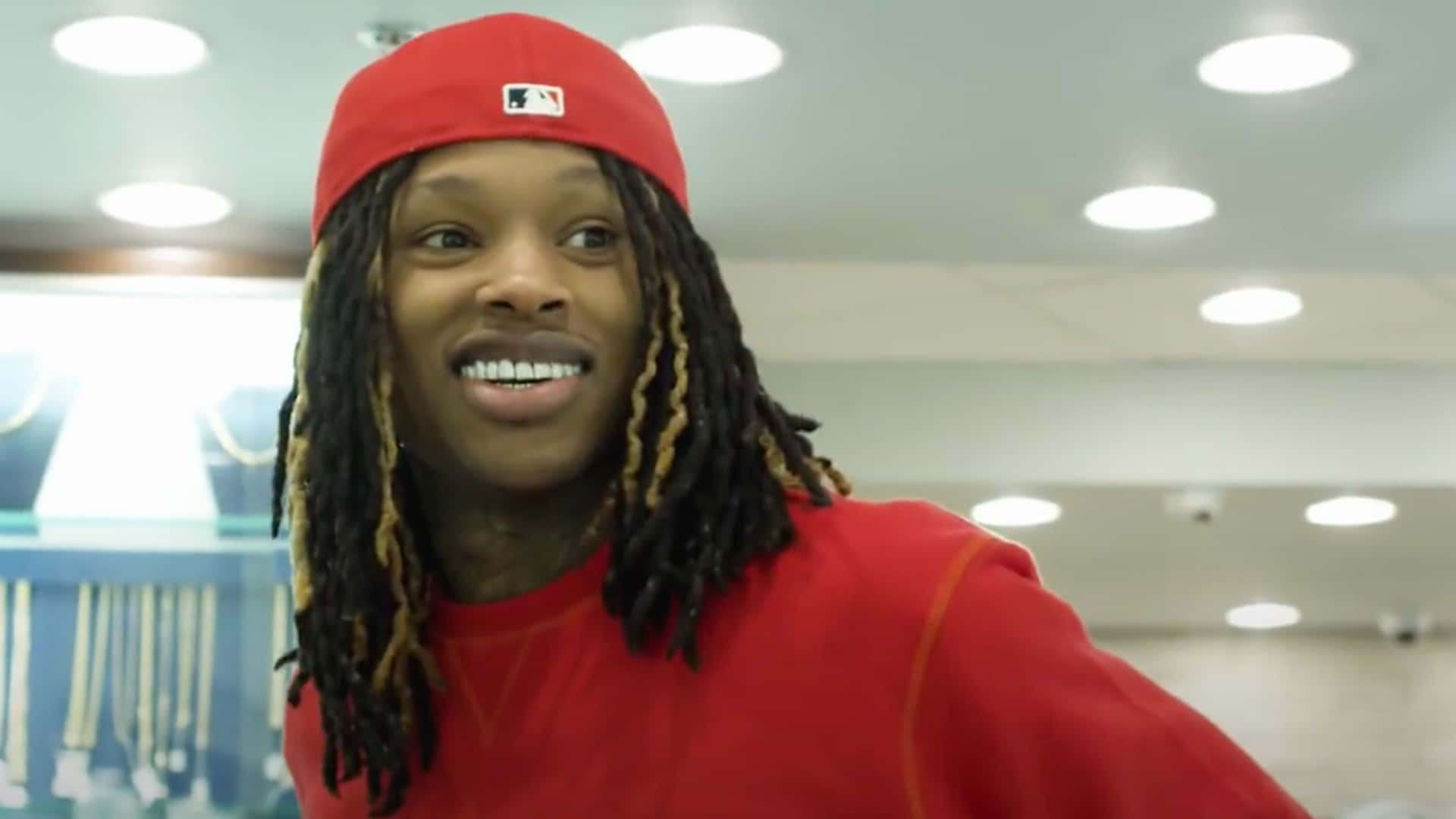 戴紅帽和辮子的年輕男子在店內微笑。 — King Von 壁紙