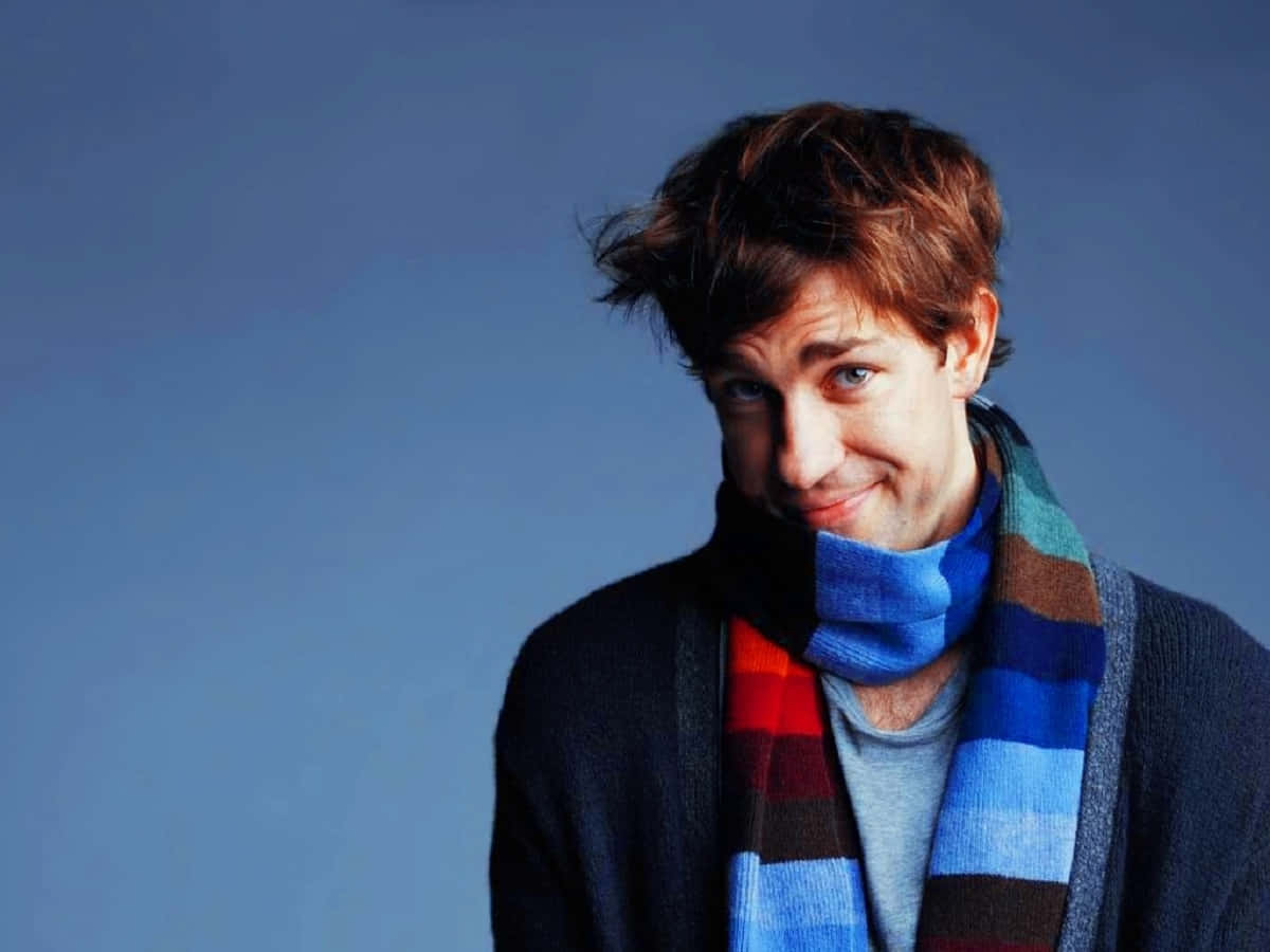 john krasinski 桌布 壁紙 — 一位年輕男子，棕色亂髮，戴著彩色條紋圍巾，在純藍色攝影棚背景前頑皮地微笑。