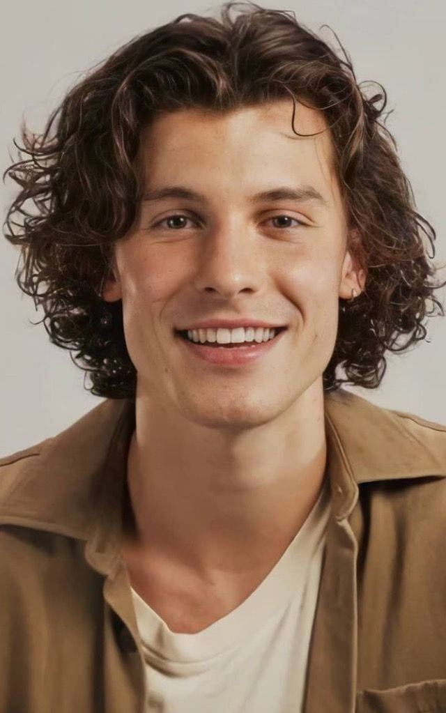 Shawn 桌布 壁紙 — 一位年輕男子，棕色捲髮，穿著米色外套內搭白襯衫，對著鏡頭溫暖微笑。