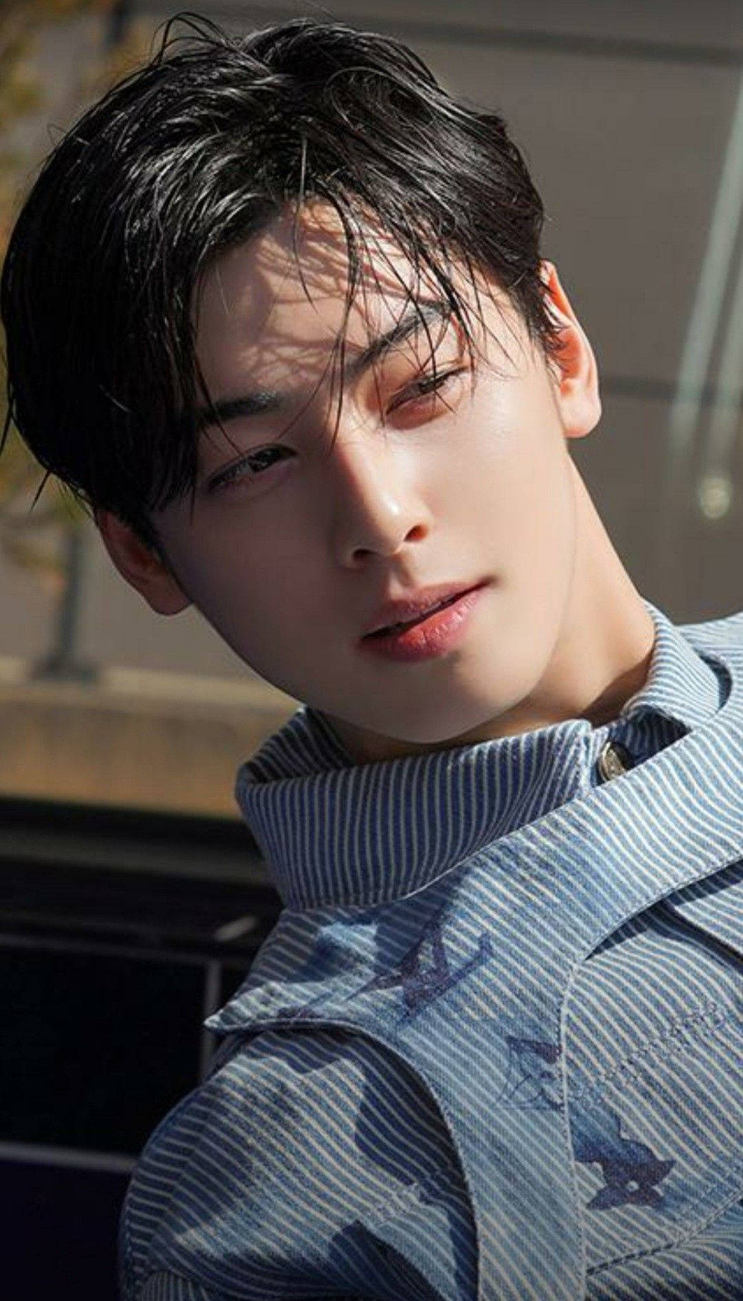 Eunwoo 桌布 壁紙 — 一位年輕男子，深色凌亂的頭髮和條紋襯衫，在溫暖的陽光下柔和地凝視著相機。