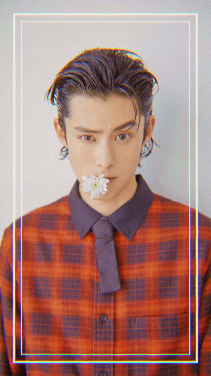 Dylan Wang 桌布 壁紙 — 一位年輕男子，深色頭髮造型時尚，身穿紅色格子襯衫，在純色背景前將一朵白花放在唇邊。