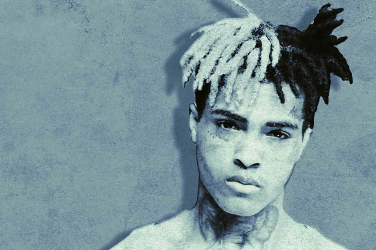 XXXTENTACION 桌布 壁紙 — 一位年輕男子，留著一半白色一半黑色的辮子，對著有紋理的藍灰色牆壁凝視。