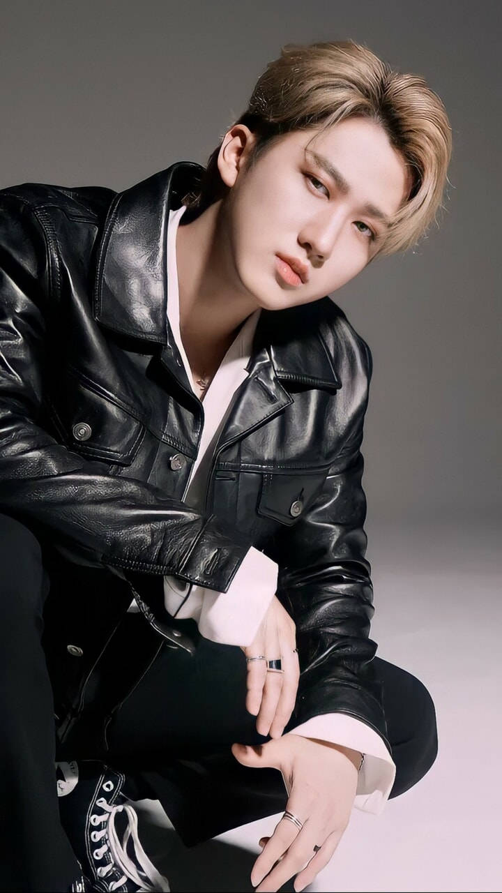 Changbin 桌布 壁紙 — 一位年輕男子，留著時尚的金色短髮，身穿黑色皮夾克內搭白襯衫，蹲在灰色中性背景前。