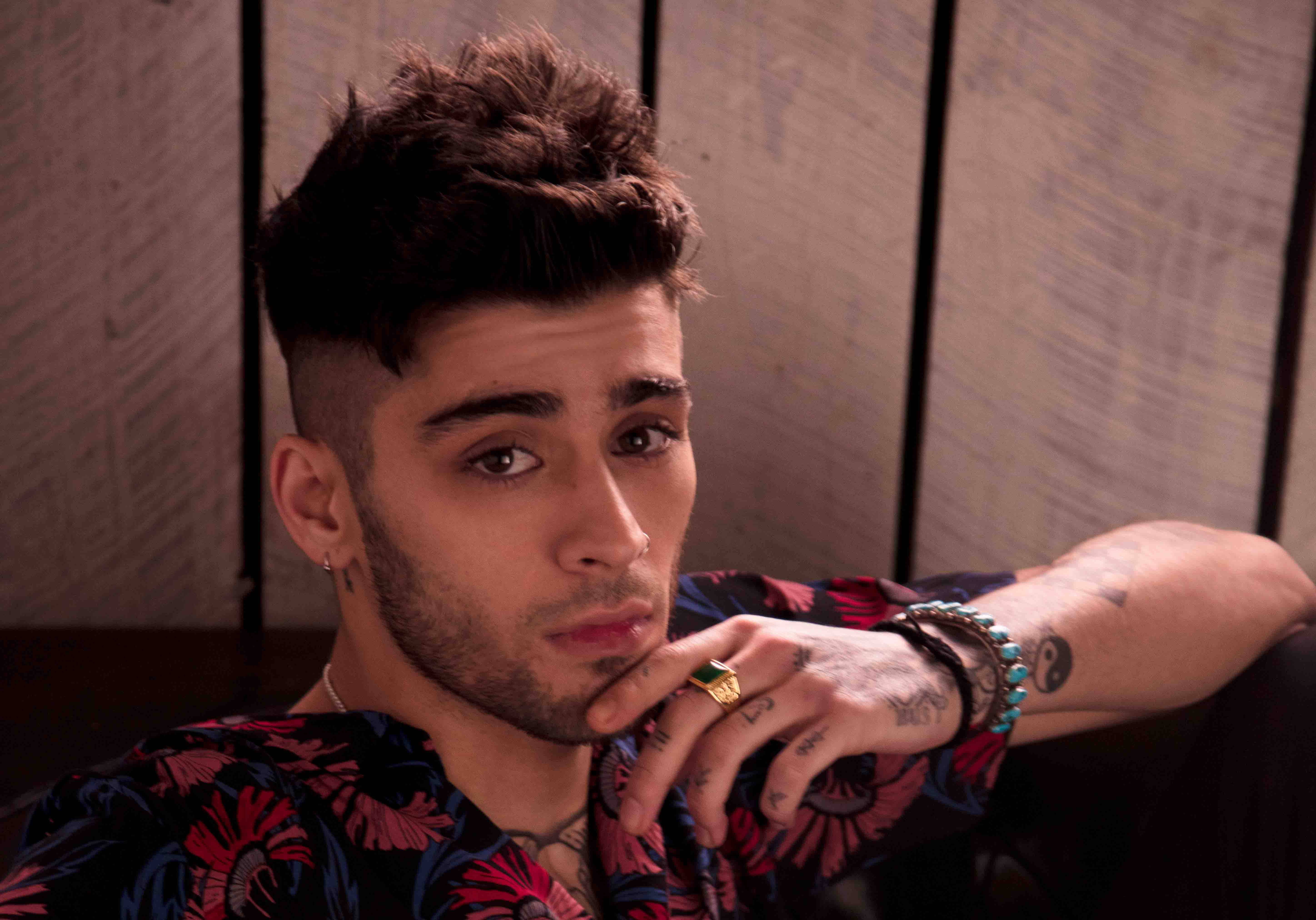 zayn 桌布 壁紙 — 一位年輕男子，留著時尚髮型並有刺青，將下巴擱在手上，靠著木鑲板牆。