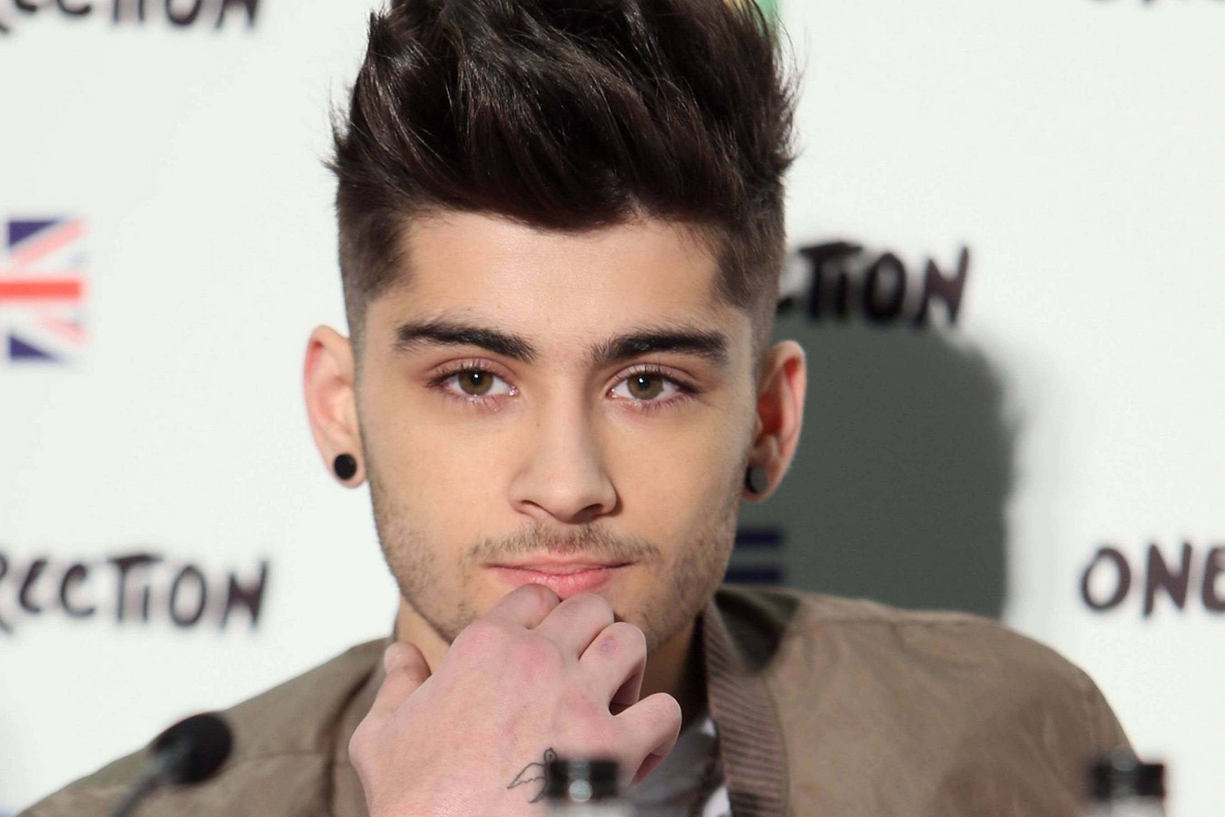 zayn 桌布 壁紙 — 一位年輕男子，留著時尚黑髮，戴著黑色耳環，在品牌背景前用手托著下巴。