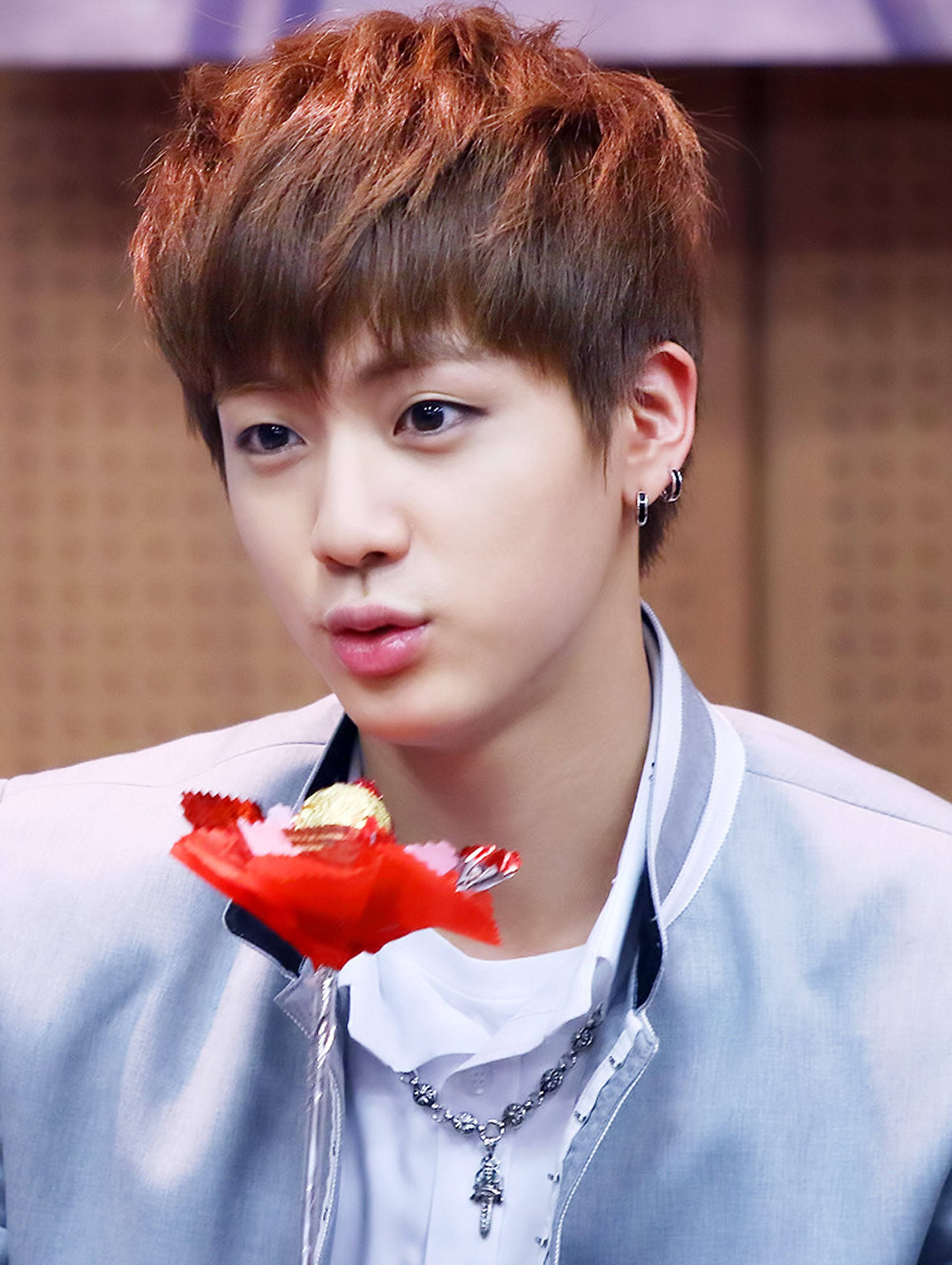 kim seok jin 桌布 壁紙 — 一位年輕男子，紅棕色頭髮，嘴裡含著一朵紅花，身穿淺藍色外套，佩戴銀飾。