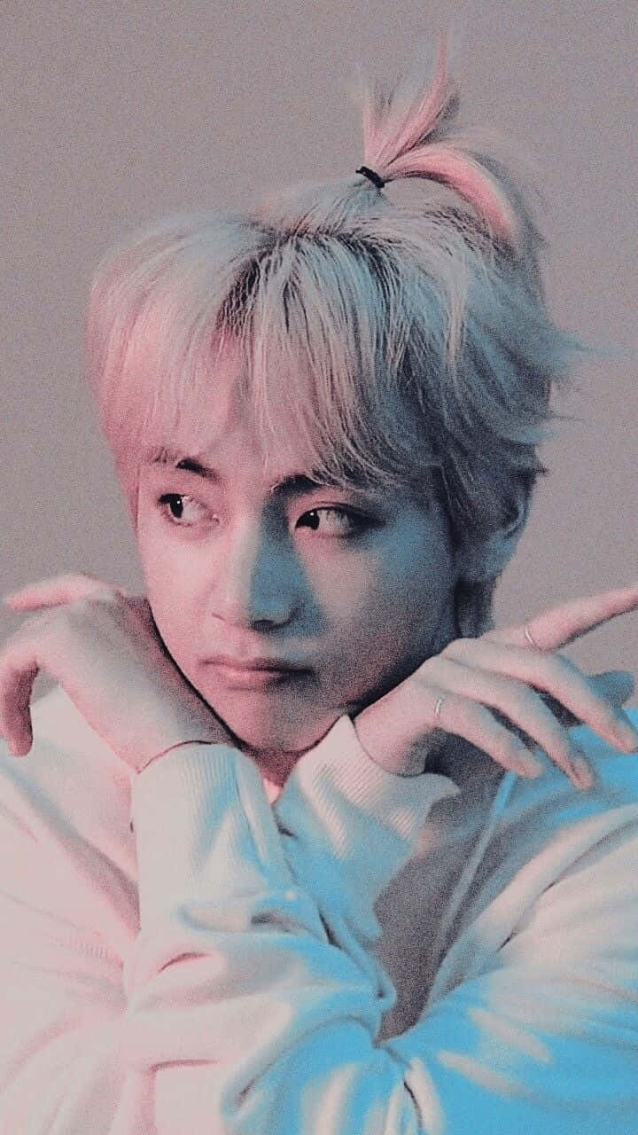 BTS V 動圖 桌布 壁紙 — 一位年輕男子，頂著粉彩粉紅和藍色頭髮紮成高髻，托腮沉思。