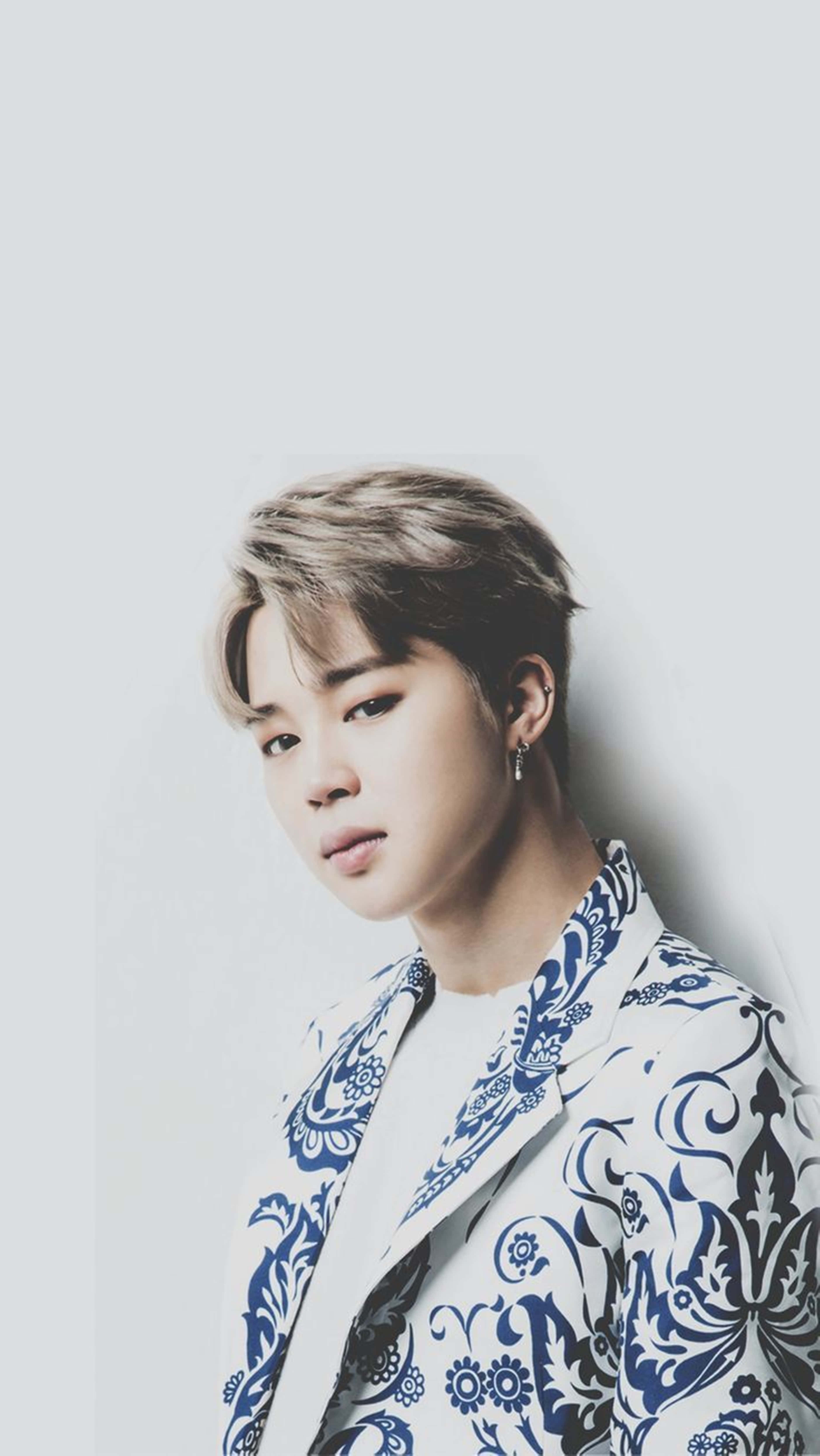 Bts Jimin 桌布 壁紙 — 一位年輕男子，頭髮造型時尚，戴著耳環，身穿藍白圖案西裝外套，背景是純淺灰色。