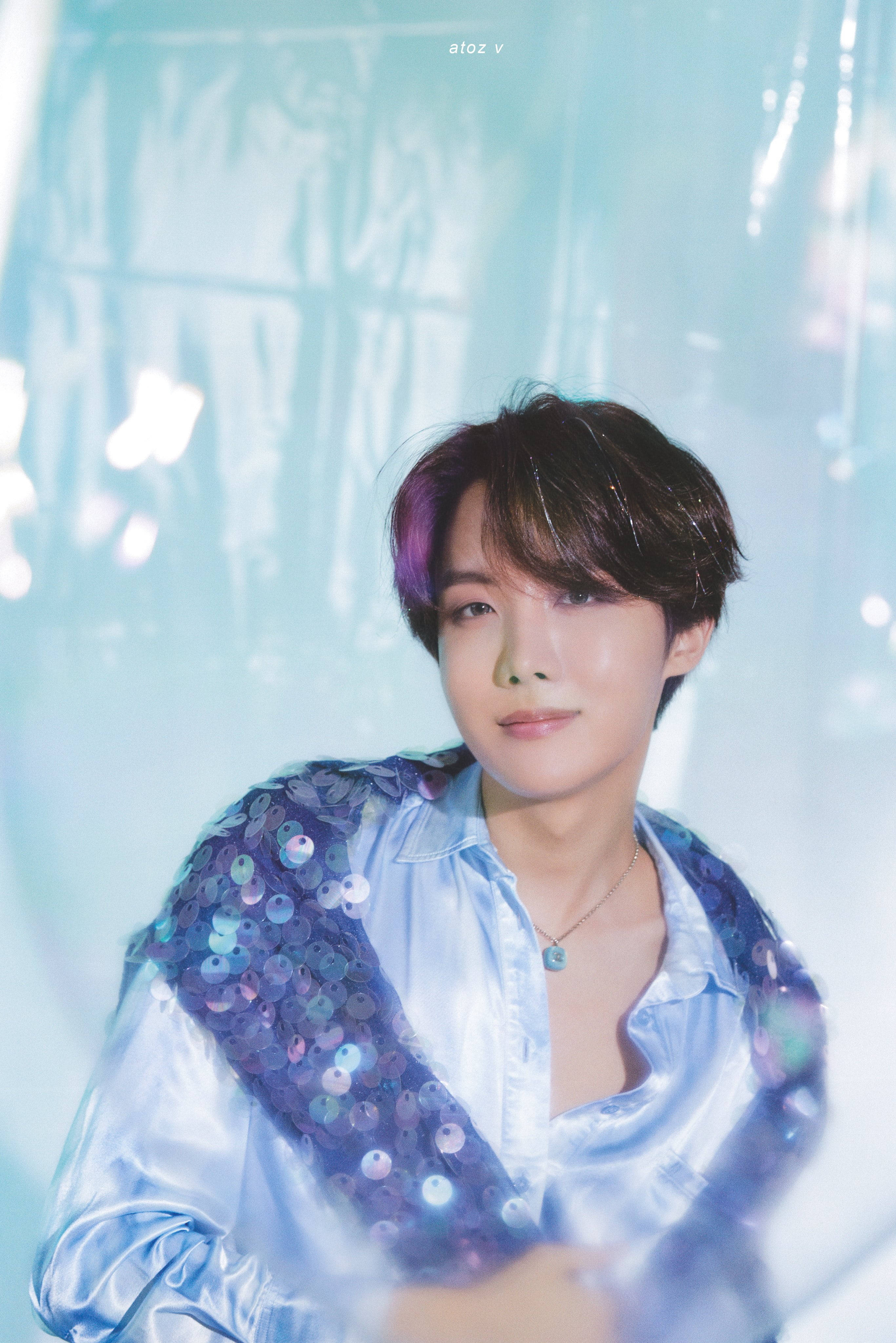 jhope 桌布 壁紙 — 一位年輕男子，髮尾帶紫色，身穿閃亮藍色珠片襯衫，背景是柔和發光的藍色。