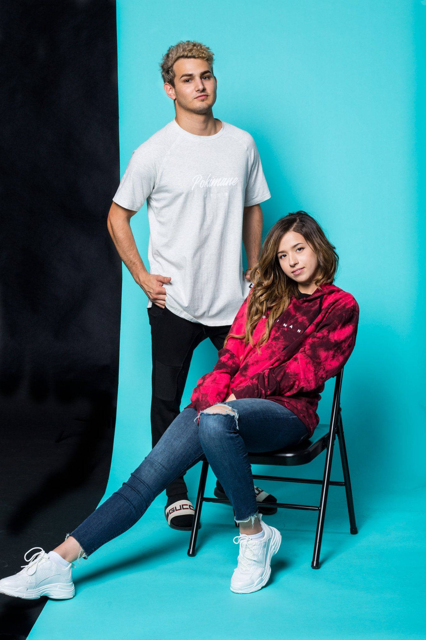 pokimane 桌布 壁紙 — 一位年輕男子和女子在鮮明的藍色和黑色工作室背景前，自信地擺出姿勢，穿著休閒街頭服飾。
