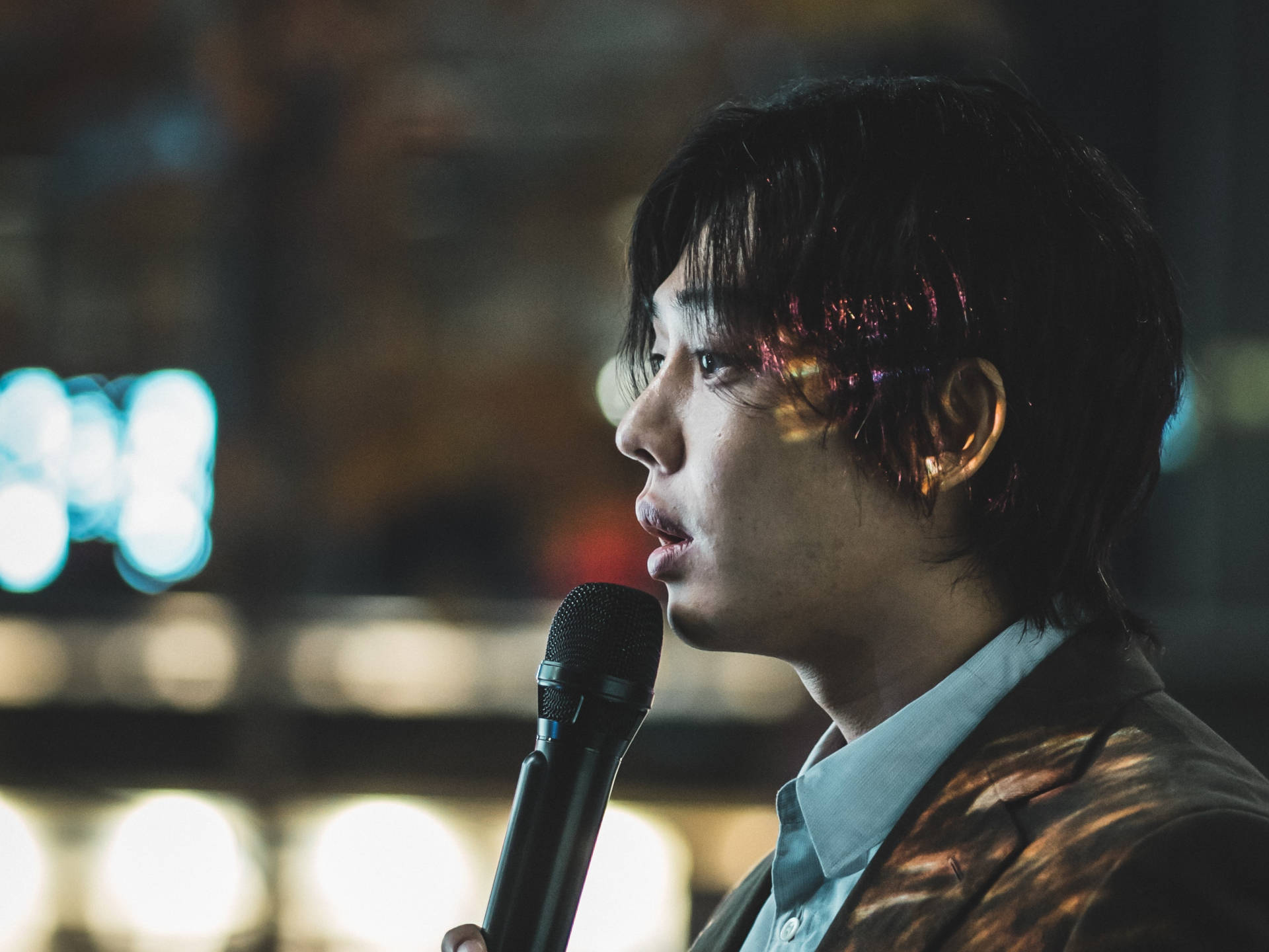 Hellbound 桌布 壁紙 — 一位年輕男子在夜晚的城市環境中，於色彩繽紛的散景燈光下對著麥克風唱歌。