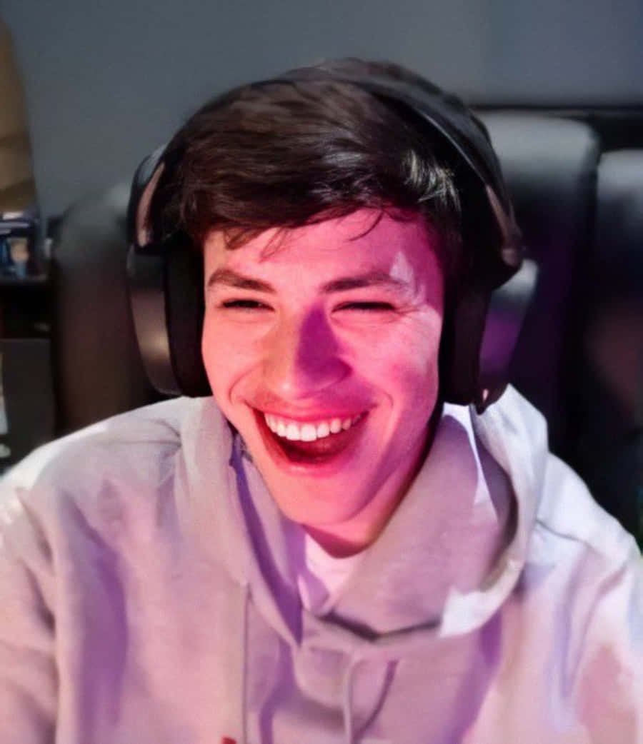 big smile 桌布 壁紙 — 一位年輕男子在昏暗的紫色環境燈光房間裡戴著耳機開懷大笑。