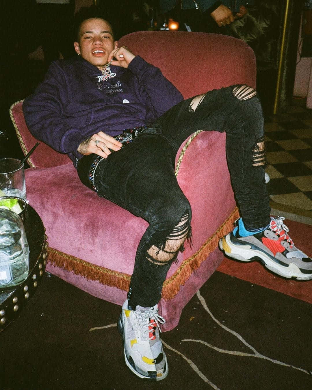 Lil Mosey 桌布 壁紙 — 一位年輕男子在燈光昏暗的房間裡，隨意地躺在一張柔軟的粉紅色扶手椅上，穿著破洞牛仔褲和色彩繽紛的運動鞋。