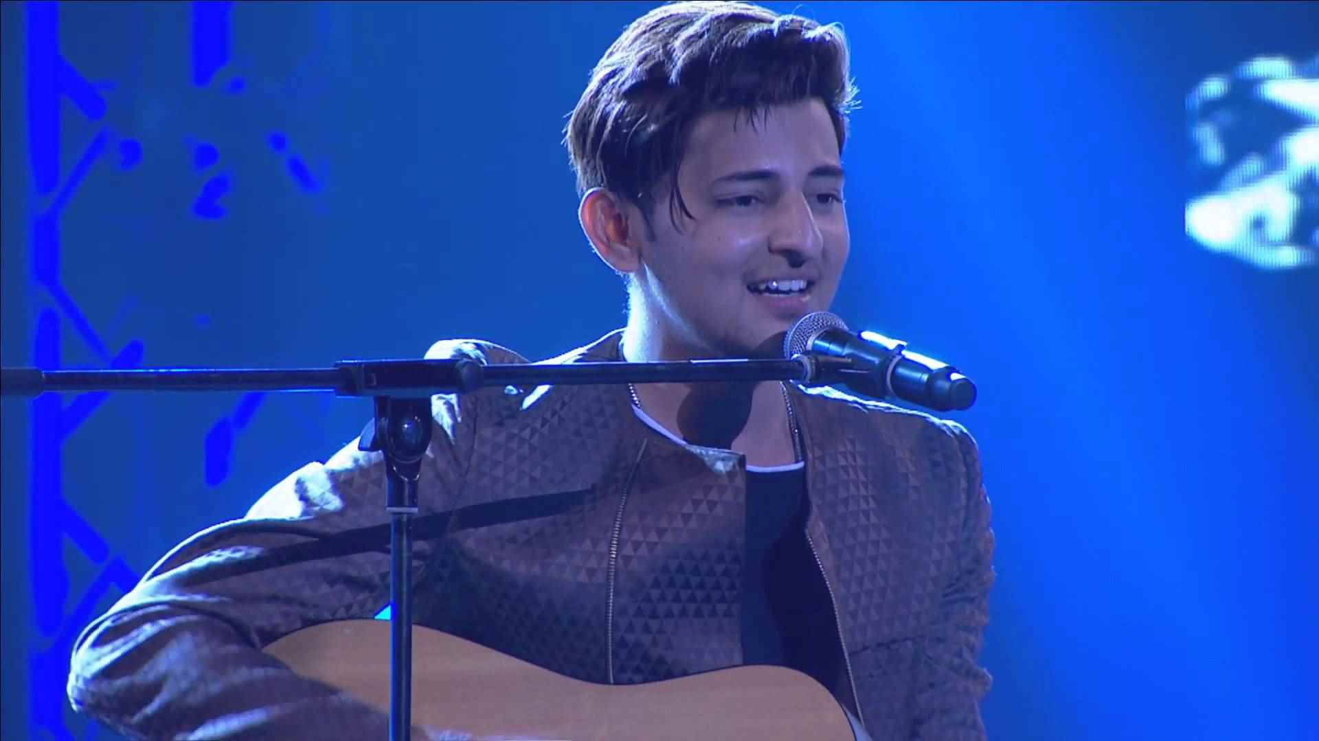 Singing 桌布 壁紙 — 一位年輕男子在藍色舞台燈光下微笑著彈吉他並對著麥克風唱歌。