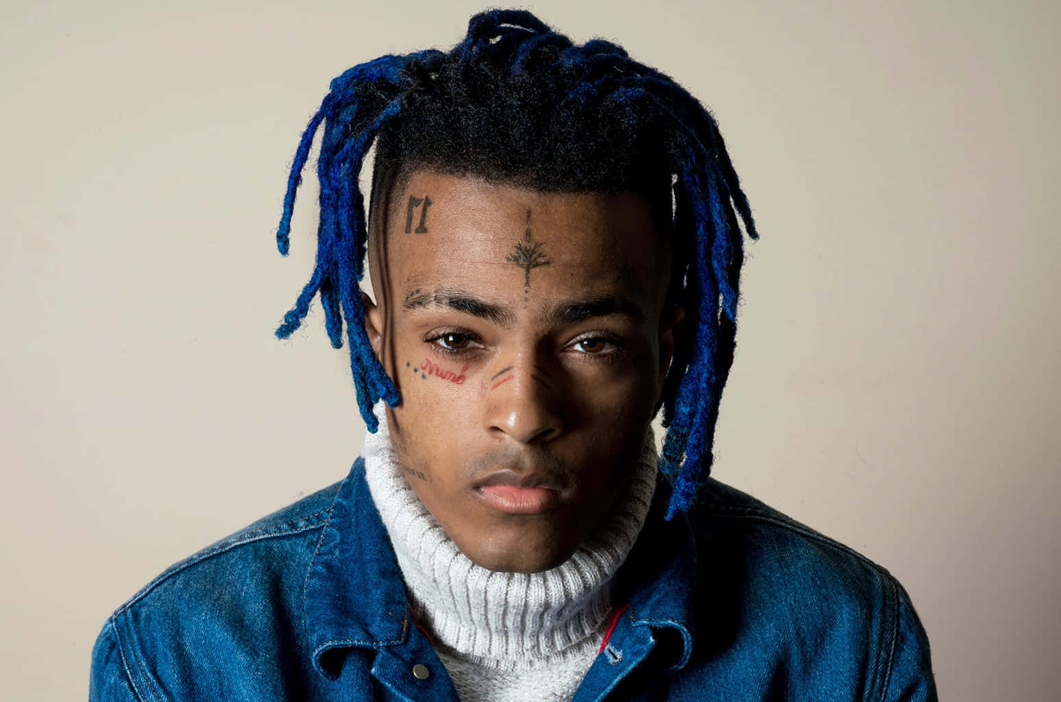 Xxxtentacion Blue Hair 桌布 壁紙 — 一位年輕男子擁有充滿活力的藍色辮子頭和臉部刺青，在純米色背景前凝視著相機。