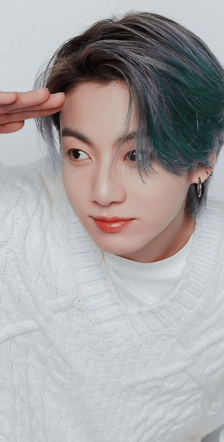 Jungkook 桌布 壁紙 — 一位年輕男子擁有引人注目的綠色和灰色頭髮，穿著白色針織毛衣，輕輕觸碰額頭。