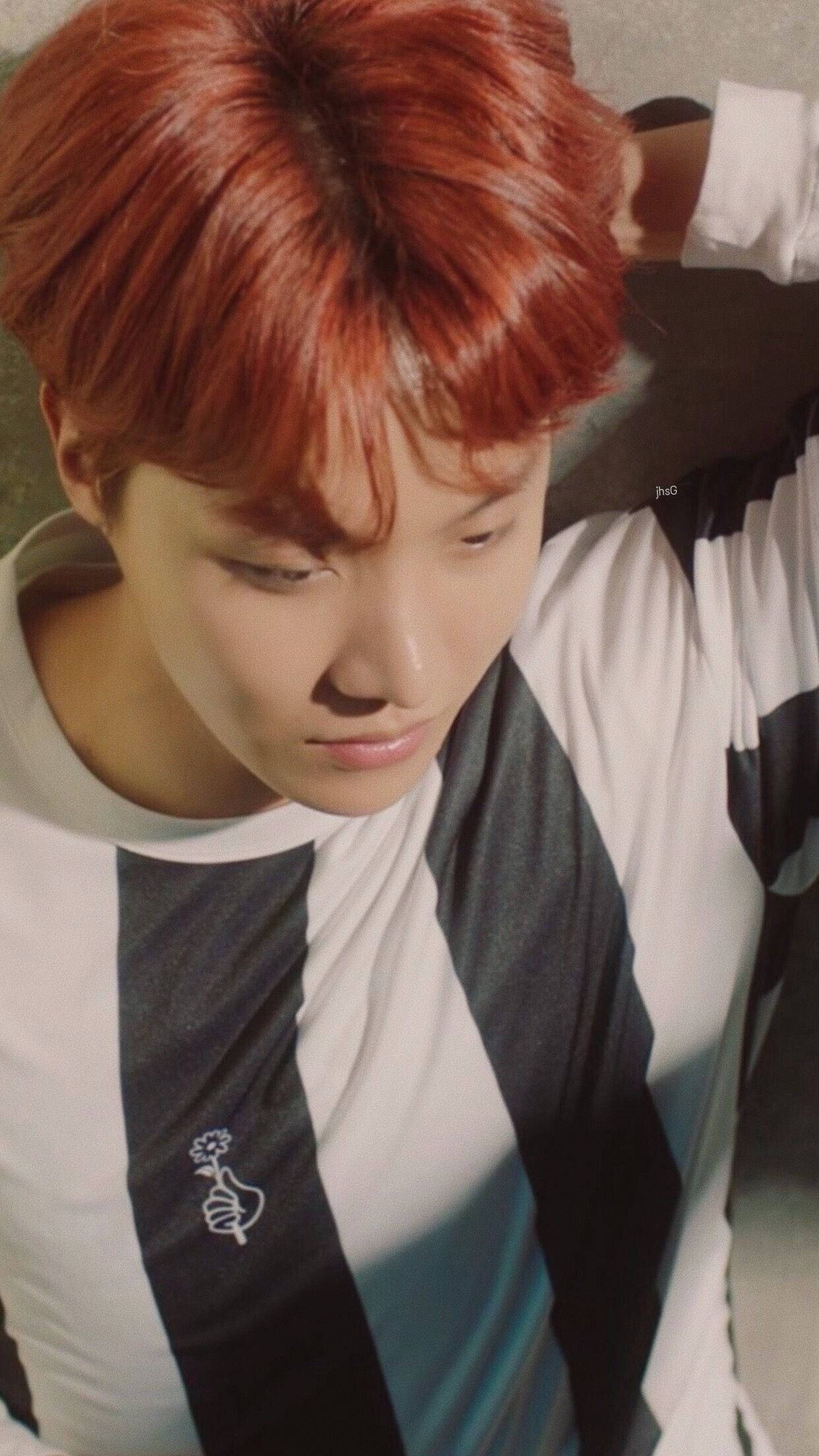 jhope 桌布 壁紙 — 一位年輕男子擁有鮮豔的紅髮，穿著黑白條紋襯衫，在溫暖的陽光下低頭。