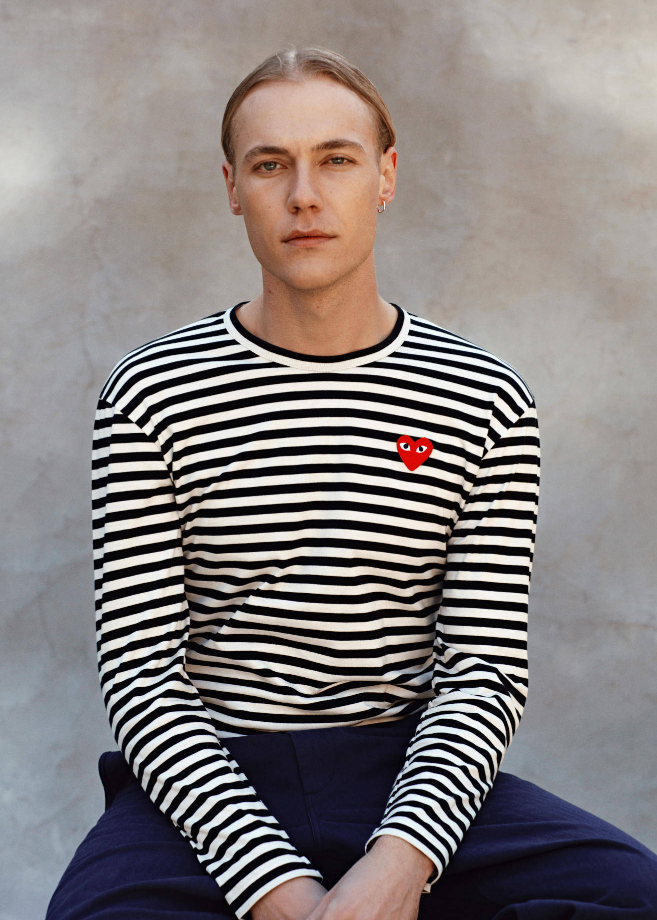 male model 桌布 壁紙 — 一位年輕男子梳著向後梳的頭髮，冷靜地坐著，身穿黑白條紋長袖襯衫，上面有紅色心形標誌。