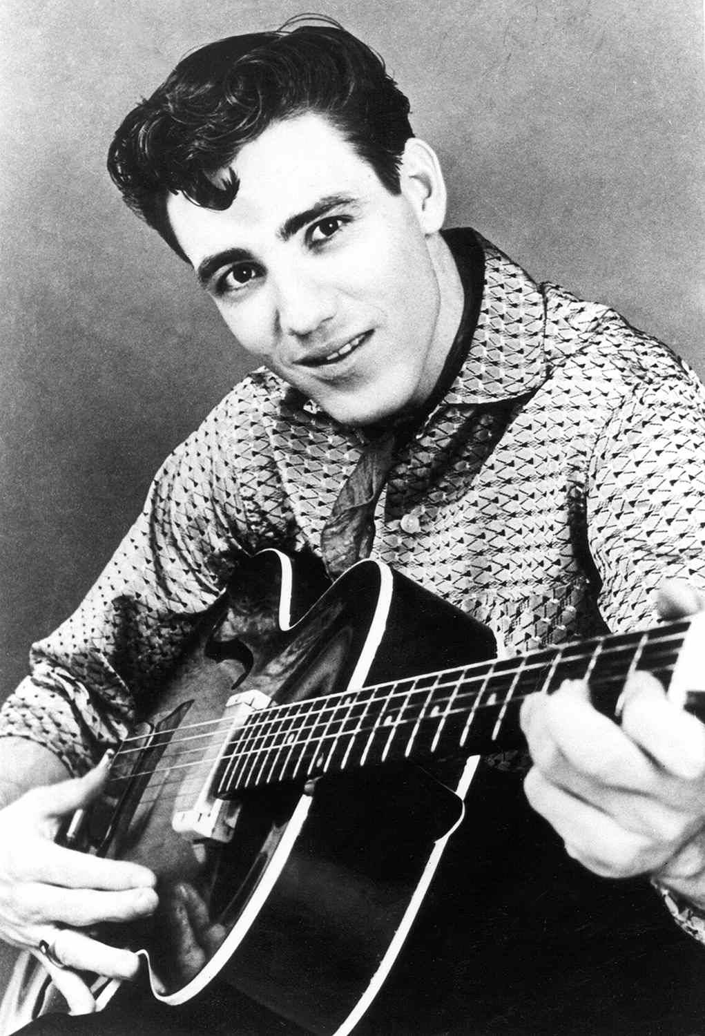 guitar player 桌布 壁紙 — 一位年輕男子梳著時尚髮型，在復古工作室肖像中微笑著抱著一把木吉他。