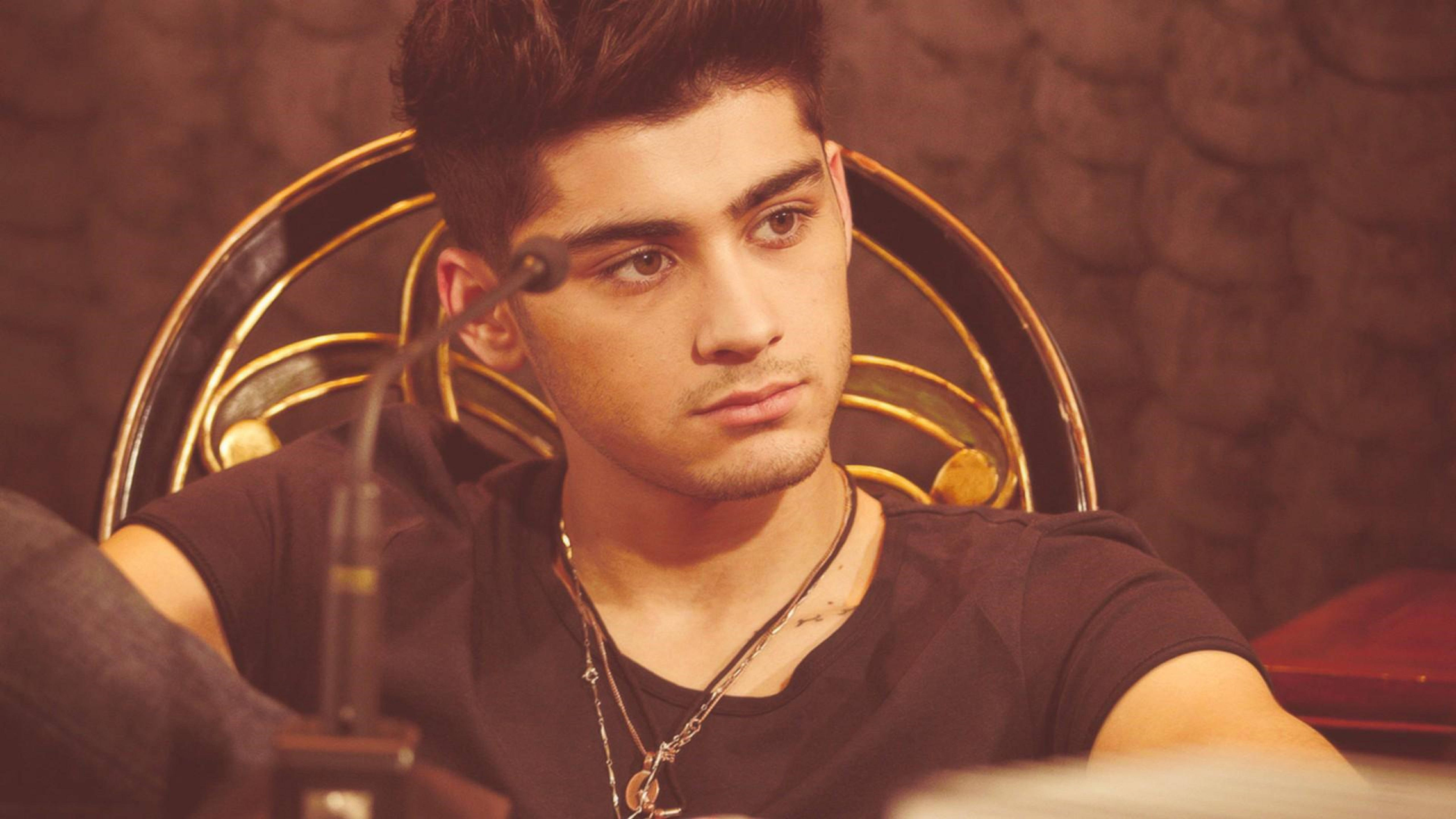 zayn 桌布 壁紙 — 一位年輕男子梳著時尚髮型，坐在金色華麗椅子上，戴著多層項鍊和黑色T恤，若有所思地望向一旁。