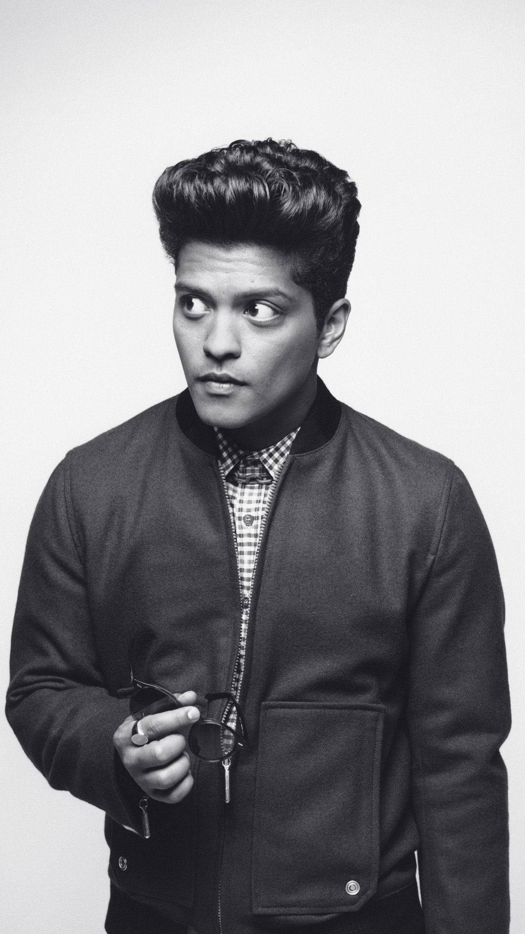Bruno Mars 桌布 壁紙 — 一位年輕男子梳著時尚髮型，手持太陽眼鏡，側視著純色黑白背景。