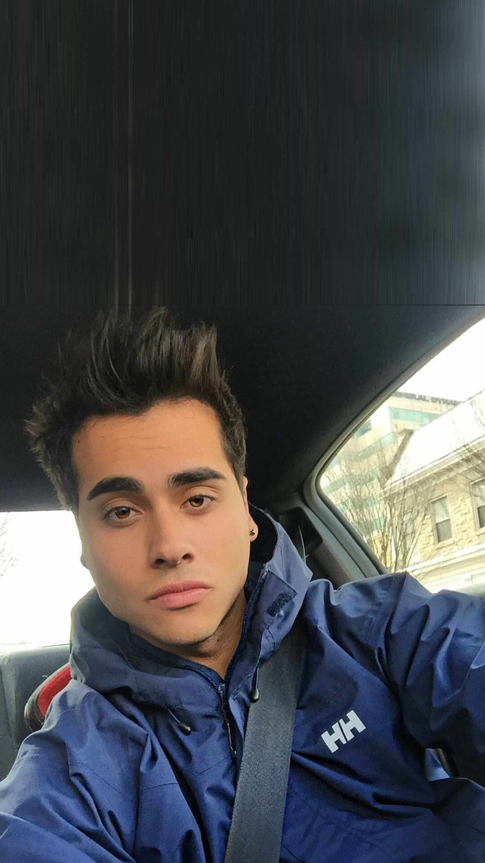 Dobre 桌布 壁紙 — 一位年輕男子梳著時尚髮型，身穿藍色Helly Hansen外套坐在車內，看著鏡頭。