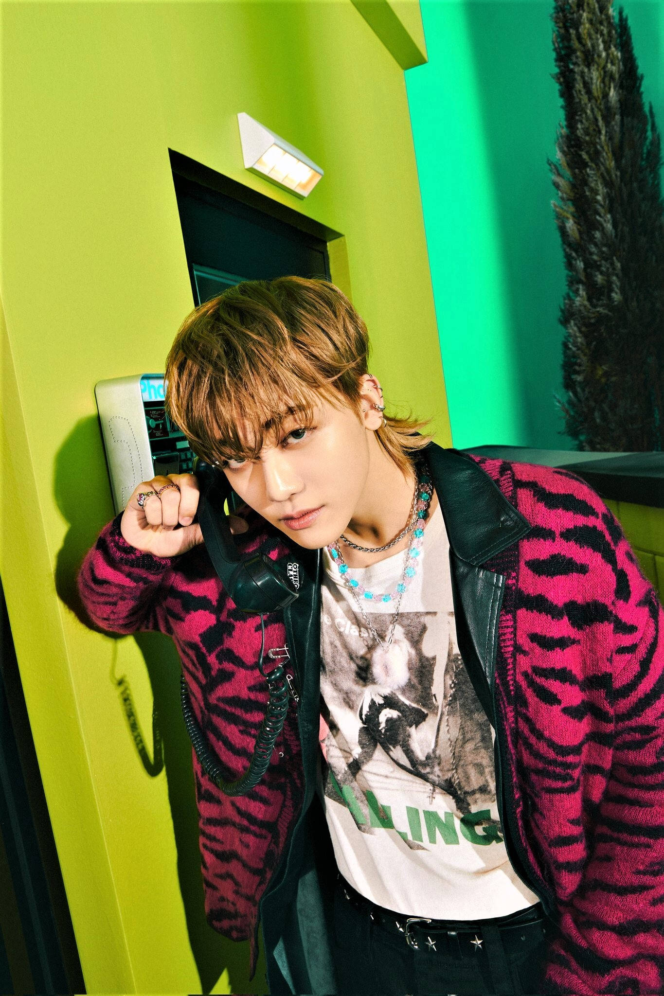 jaemin 桌布 壁紙 — 一位年輕男子梳著時尚髮型，靠著充滿活力的萊姆綠色牆壁，手持復古電話，眼神專注。