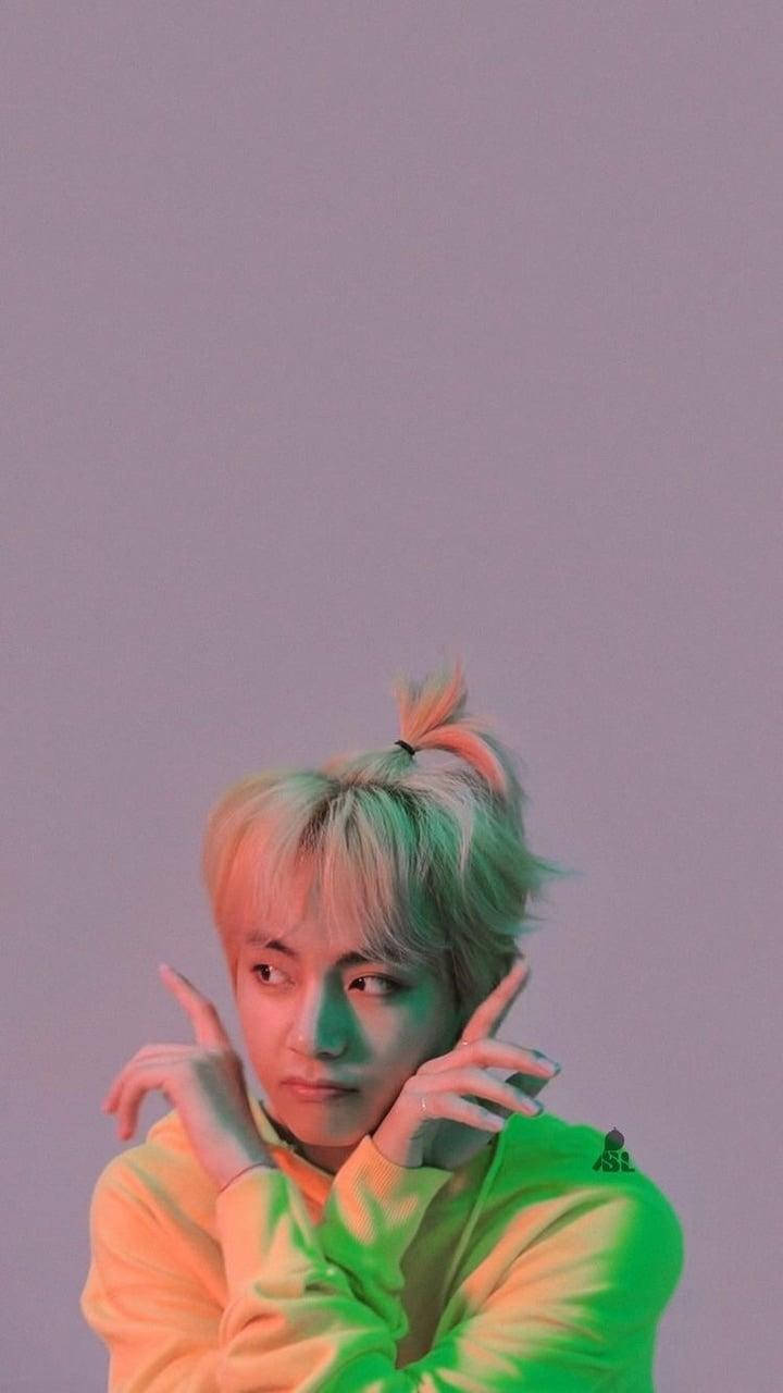 Taehyung Cute 桌布 壁紙 — 一位年輕男子梳著粉彩髮髻，在霓虹綠和橙色燈光下，以薰衣草牆為背景擺姿勢。