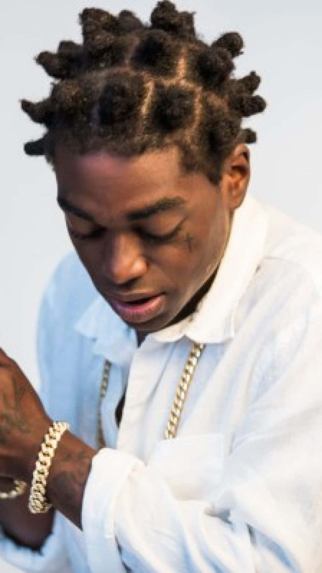 Rappers 桌布 壁紙 — 一位年輕男子梳著精緻辮子，戴著金鍊，在極簡風格的攝影棚照中向下凝視。