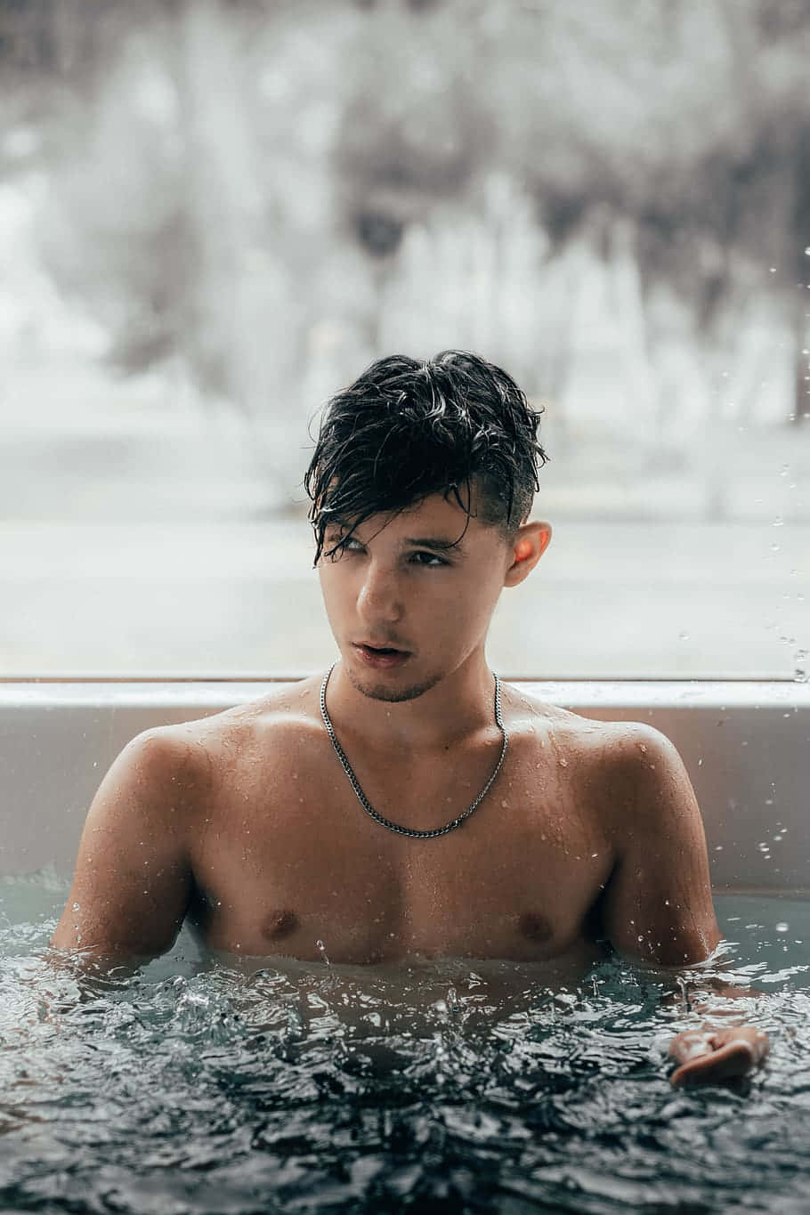 Hot Guy 桌布 壁紙 — 一位年輕男子濕著深色頭髮坐在浴缸中，水花四濺，背景是模糊的雪景窗戶。
