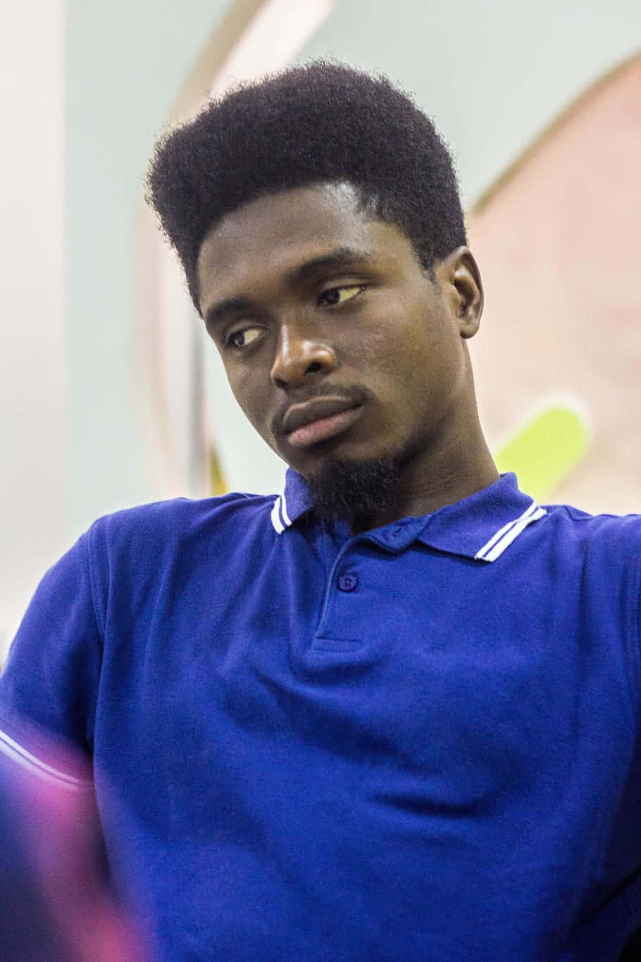 Nigeria 桌布 壁紙 — 一位年輕男子留著整齊的非洲式髮型和山羊鬍，身穿皇家藍色Polo衫，若有所思地望向一旁。