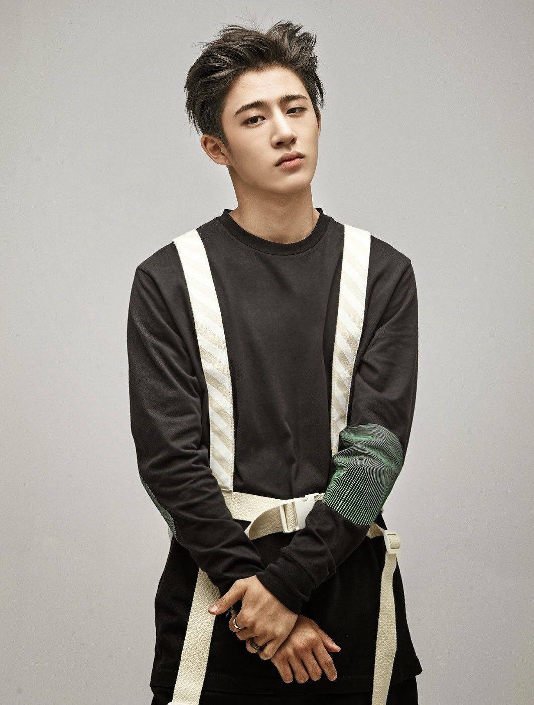 kim hanbin 桌布 壁紙 — 一位年輕男子留著時尚深色頭髮，身穿黑色長袖襯衫，搭配白色吊帶和綠色圖案袖子，背景為純灰色。