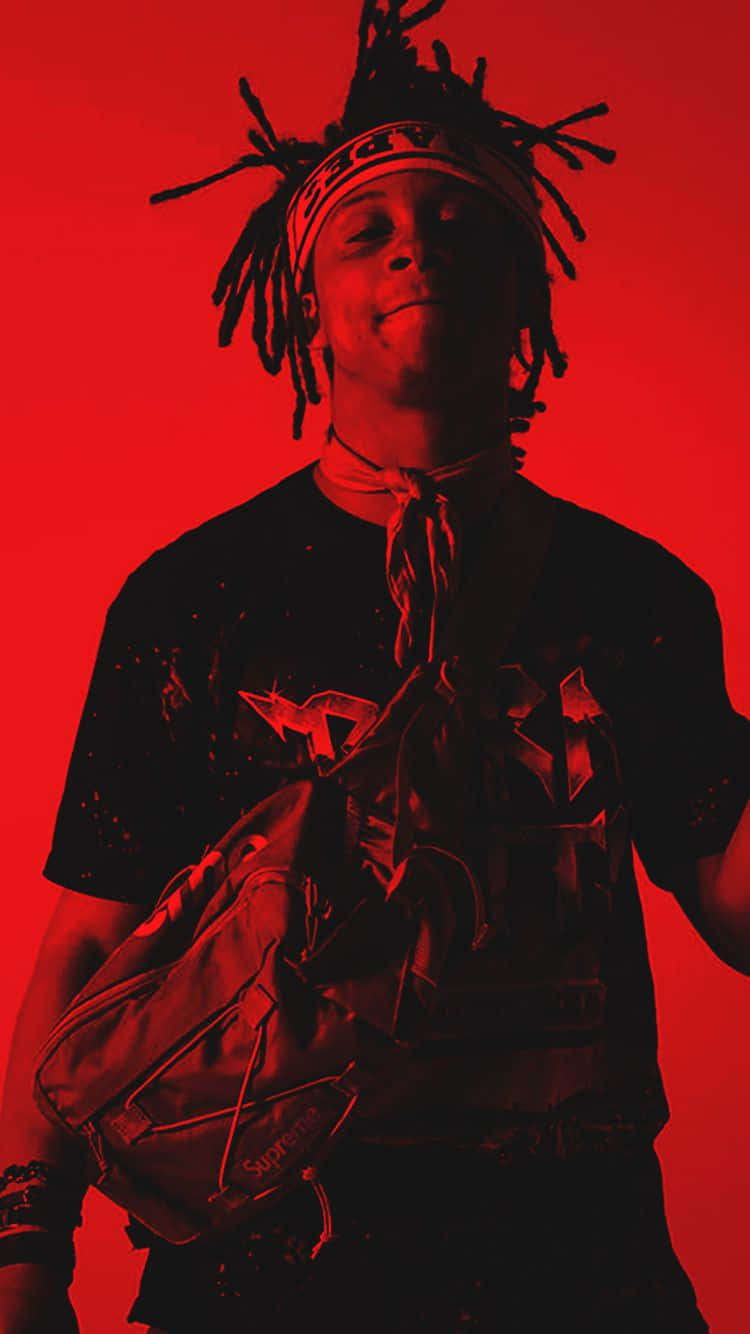 Trippie Redd 桌布 壁紙 — 一位年輕男子留著辮子頭、戴著頭帶，在飽和的紅色背景前自信微笑。