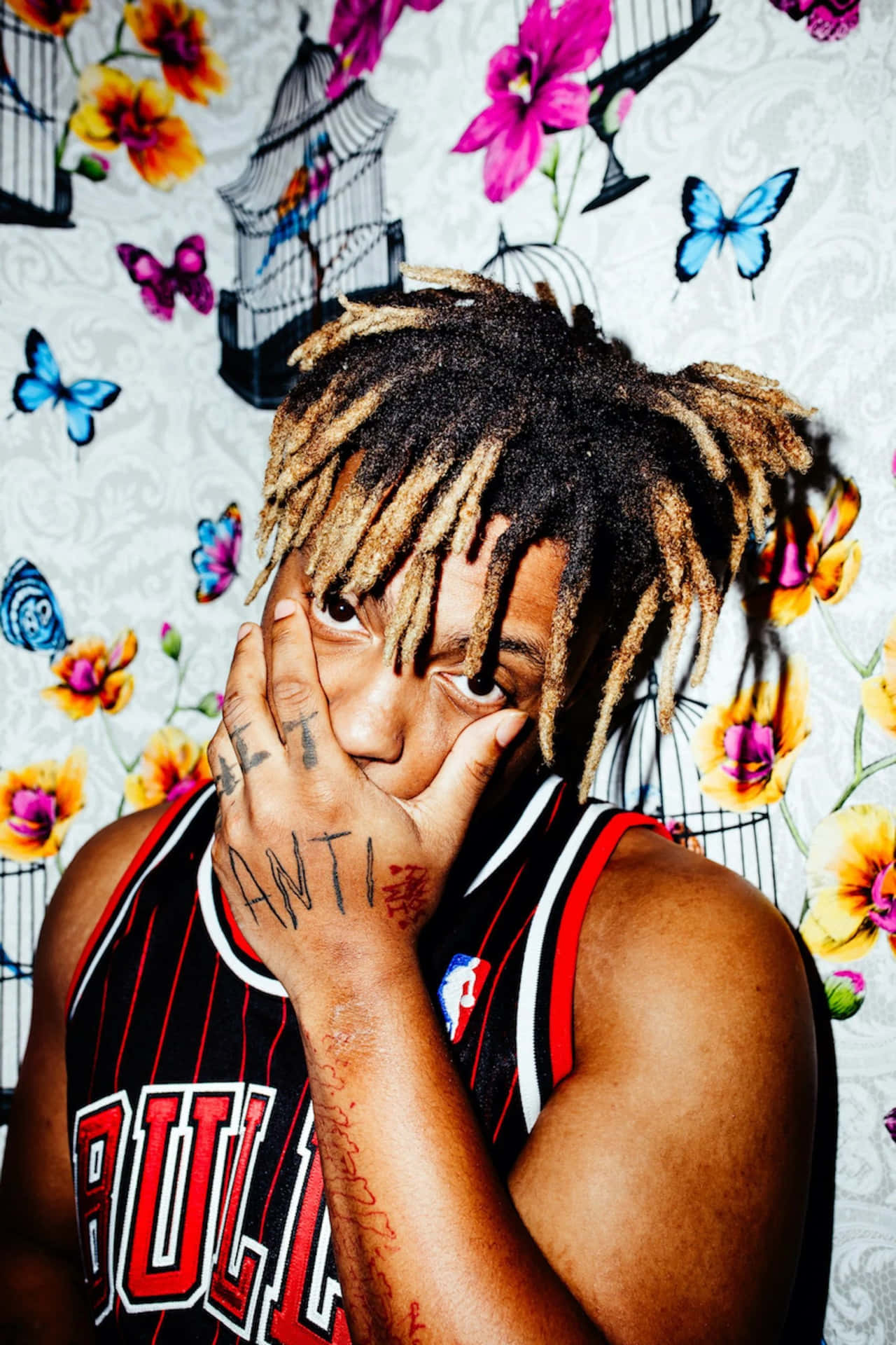 年輕男子留著辮子頭和刺青，在花卉壁紙前遮住臉。 — Juice Wrld 壁紙