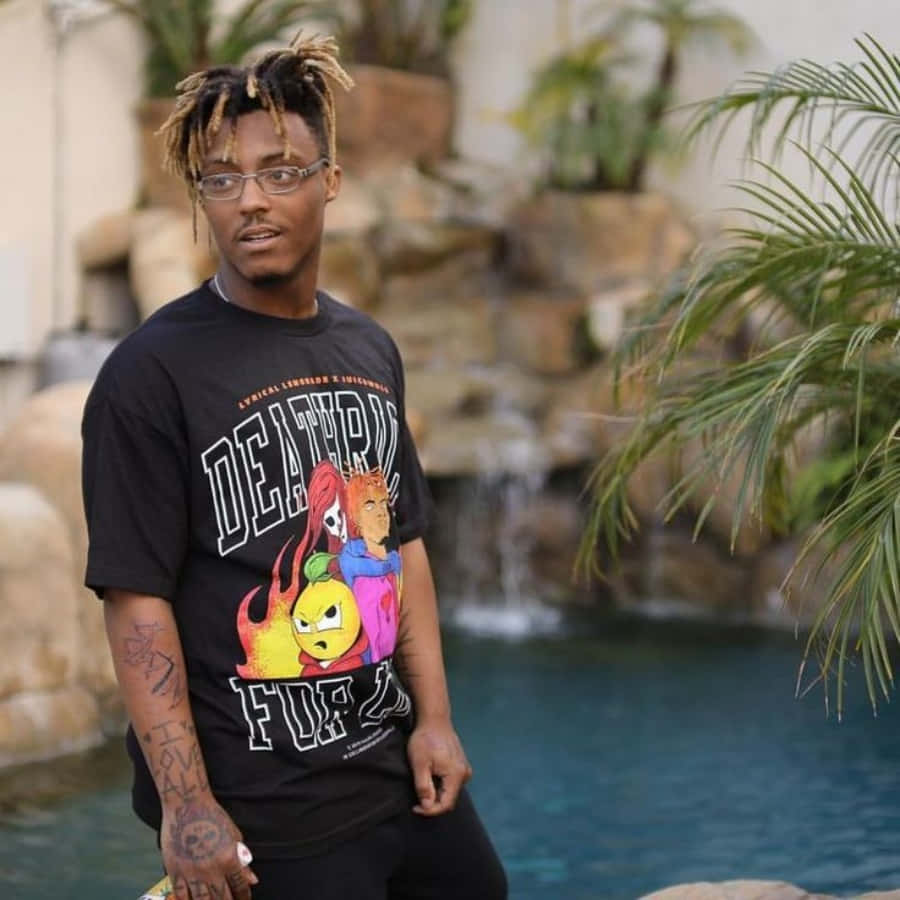 年輕男子留著辮子頭戴眼鏡，站在有瀑布的泳池旁。 — Juice Wrld 壁紙