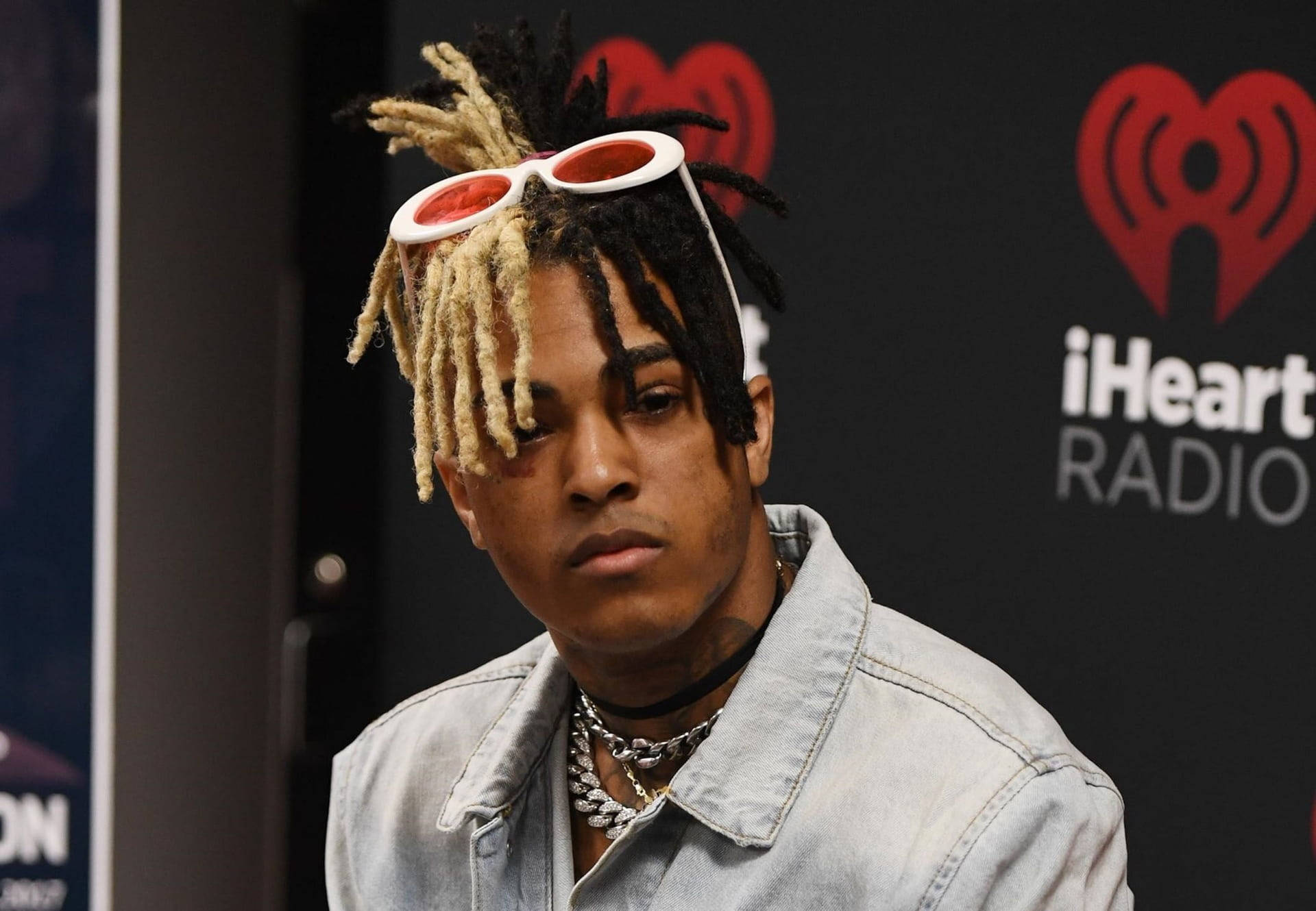 xxxtentacion 電腦 桌布 壁紙 — 一位年輕男子留著金色和黑色辮子，頭戴白色太陽眼鏡，身穿牛仔外套，出席iHeartRadio活動。