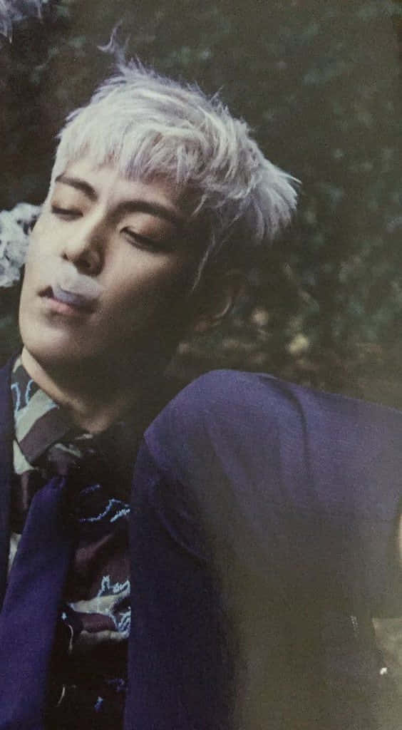 big bang 桌布 壁紙 — 一位年輕男子留著鉑金色頭髮，穿著紫色西裝，在模糊的綠色背景前呼出煙霧。