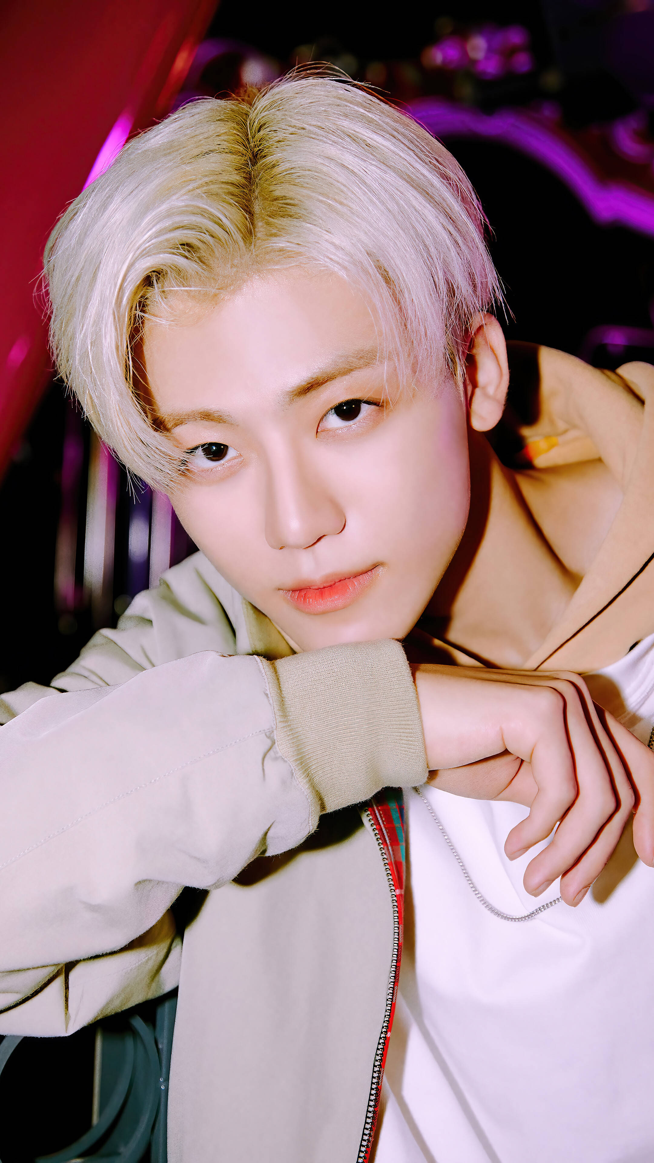 jaemin 桌布 壁紙 — 一位年輕男子留著鉑金色頭髮，穿著連帽衫，在鮮紅和紫色舞台燈光下向前傾身。