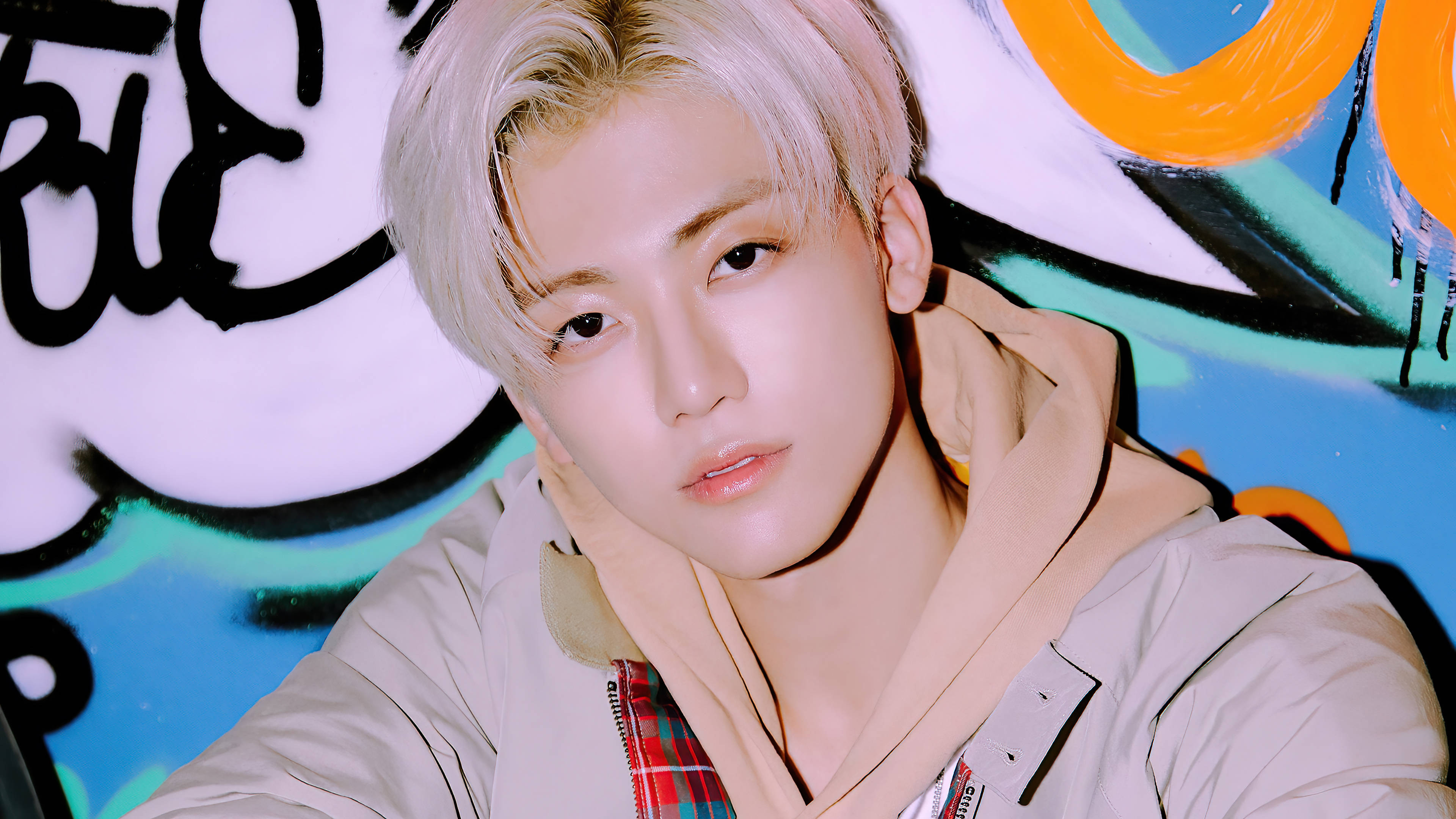 jaemin 桌布 壁紙 — 一位年輕男子留著鉑金色頭髮，身穿米色連帽上衣，背景是充滿活力的塗鴉牆，上面有醒目的橙色、藍綠色和黑色漩渦圖案。