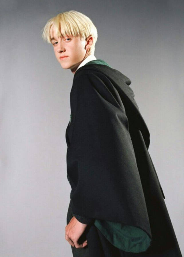 draco 桌布 壁紙 — 一位年輕男子留著鉑金色頭髮，身穿深色長袍，內搭綠色和銀色服飾，在純灰色背景前轉頭回望。