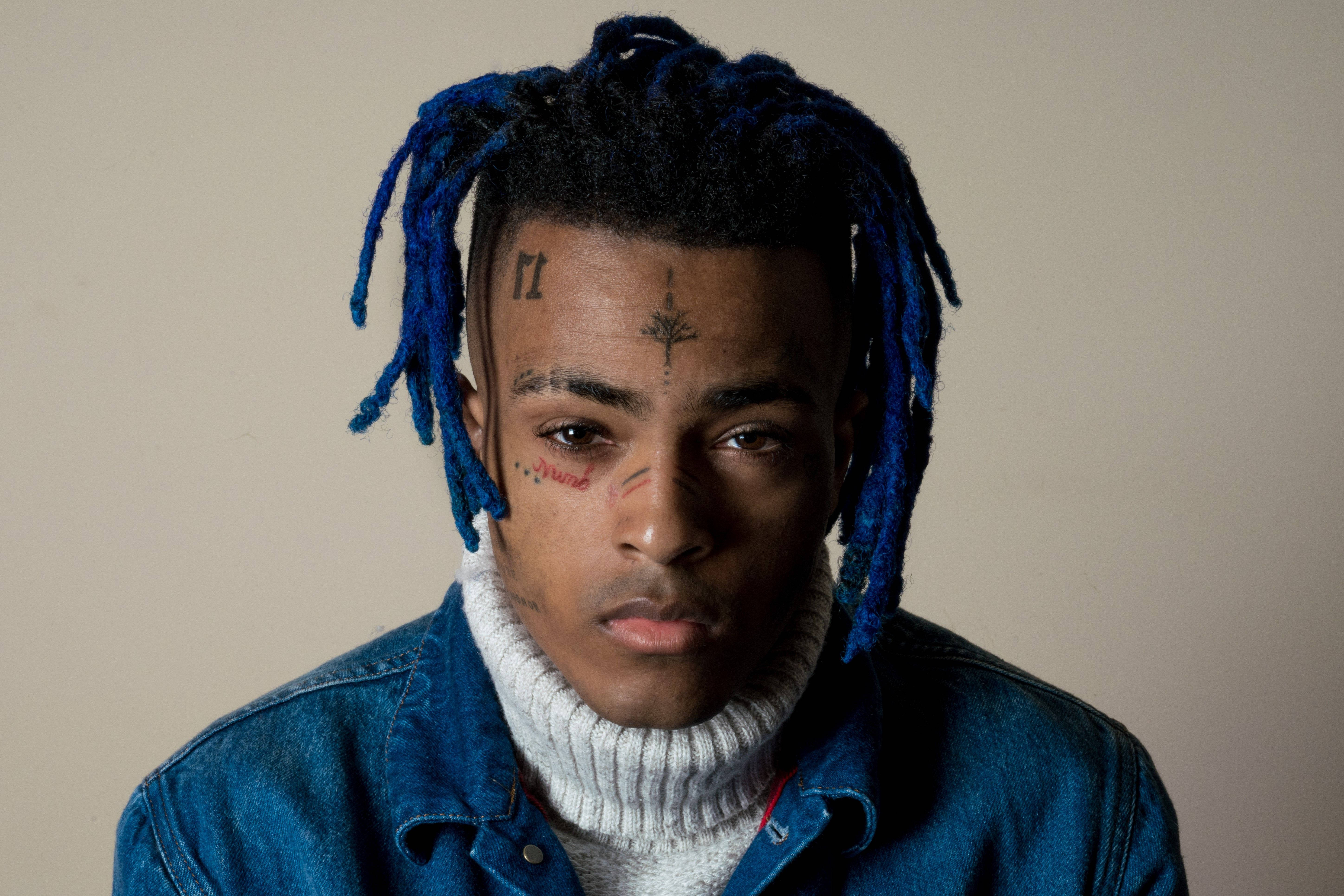 xxxtentacion 動畫 桌布 壁紙 — 一位年輕男子的特寫肖像，他有藍色辮子頭和臉部刺青，穿著牛仔外套內搭白色高領衫。