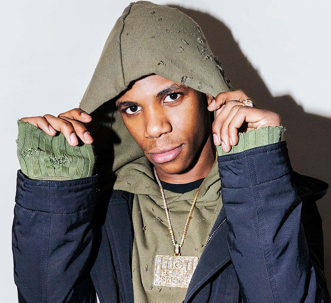 Rappers 桌布 壁紙 — 一位年輕男子穿著破舊的橄欖綠色連帽衫和深色外套，拉起帽子，專注地看著鏡頭。