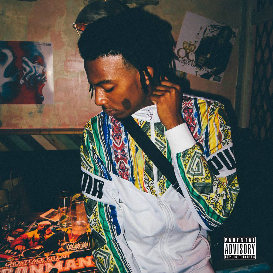 Carti 桌布 壁紙 — 一位年輕男子穿著鮮豔圖案外套，在燈光昏暗的房間裡調整耳機，房間裝飾著嘻哈海報和家長指引貼紙。