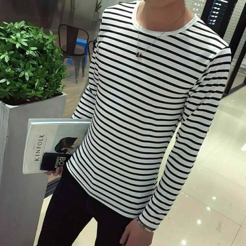 clothing 桌布 壁紙 — 一位年輕男子穿著黑白條紋長袖襯衫，在現代室內環境中拿著雜誌靠近盆栽植物。