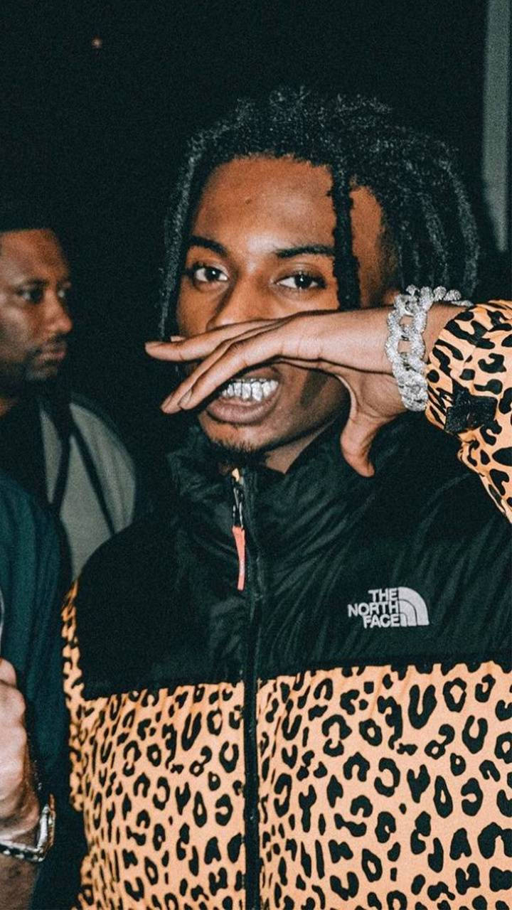 Carti 桌布 壁紙 — 一位年輕男子編著辮子，微笑著用手遮住嘴巴，身穿豹紋外套。