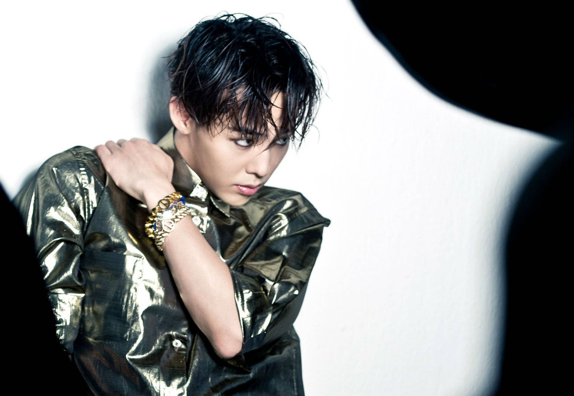 G-dragon 桌布 壁紙 — 一位年輕男子身穿閃亮金色外套，在純白背景前擺出戲劇性姿勢，帶有鮮明黑色陰影。