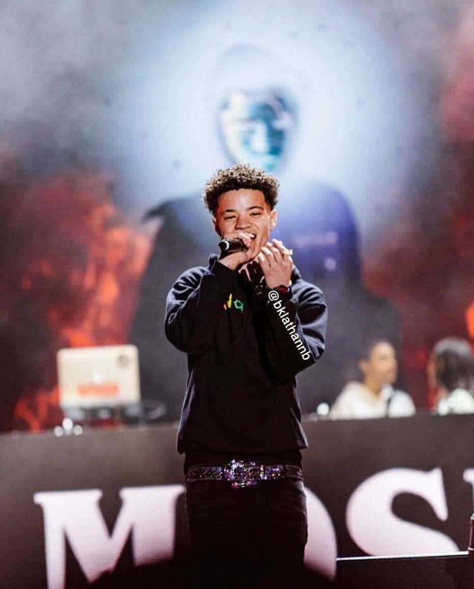 Lil Mosey 桌布 壁紙 — 一位年輕男表演者在煙霧瀰漫的舞台上，在火紅與冷藍燈光下，對著麥克風熱情獻唱。