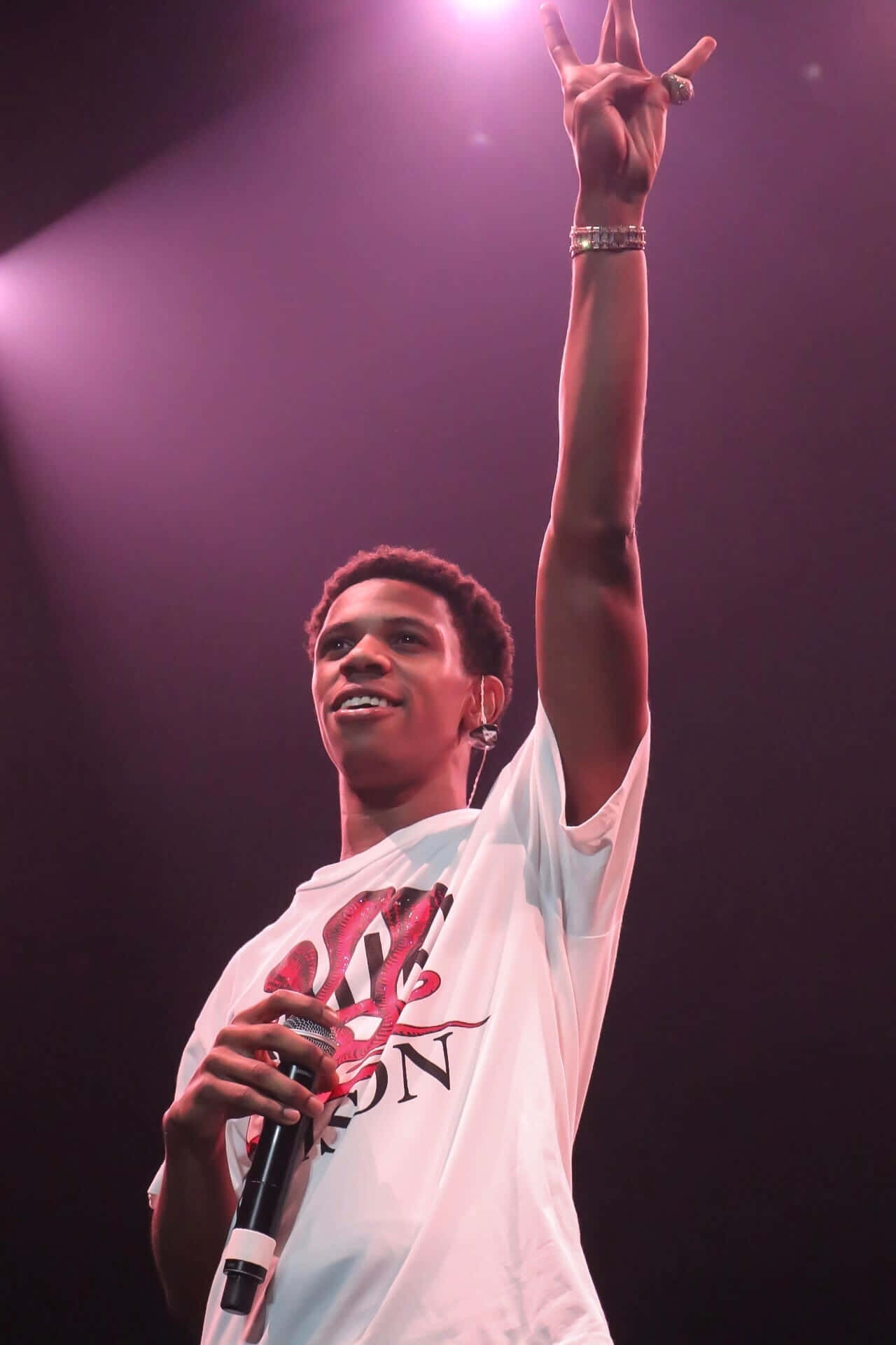 A Boogie Wit Da Hoodie 桌布 壁紙 — 一位年輕男表演者在紫色聚光燈下燦爛微笑，手持麥克風，舉起手做出和平手勢。