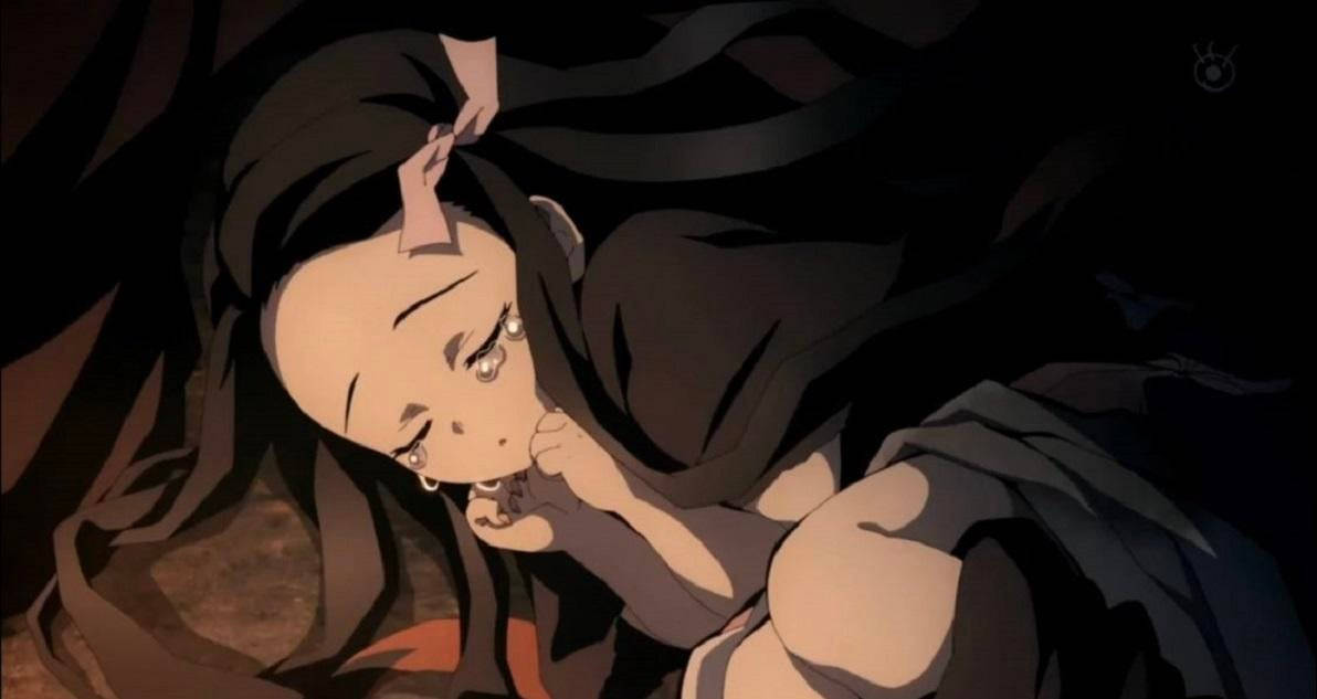 鬼滅之刃 禰豆子 桌布 壁紙 — 一位年輕的動漫女孩，深色頭髮，淚眼汪汪，在昏暗的場景中將頭靠在手上。