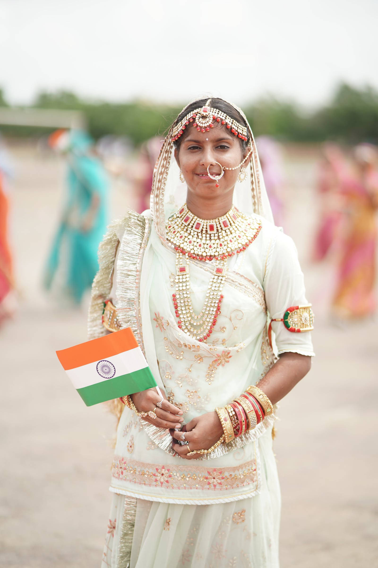 Tiranga 桌布 壁紙 — 一位年輕的印度女性身穿華麗的白色傳統服飾和黃金首飾，手持印度國旗對著鏡頭微笑。